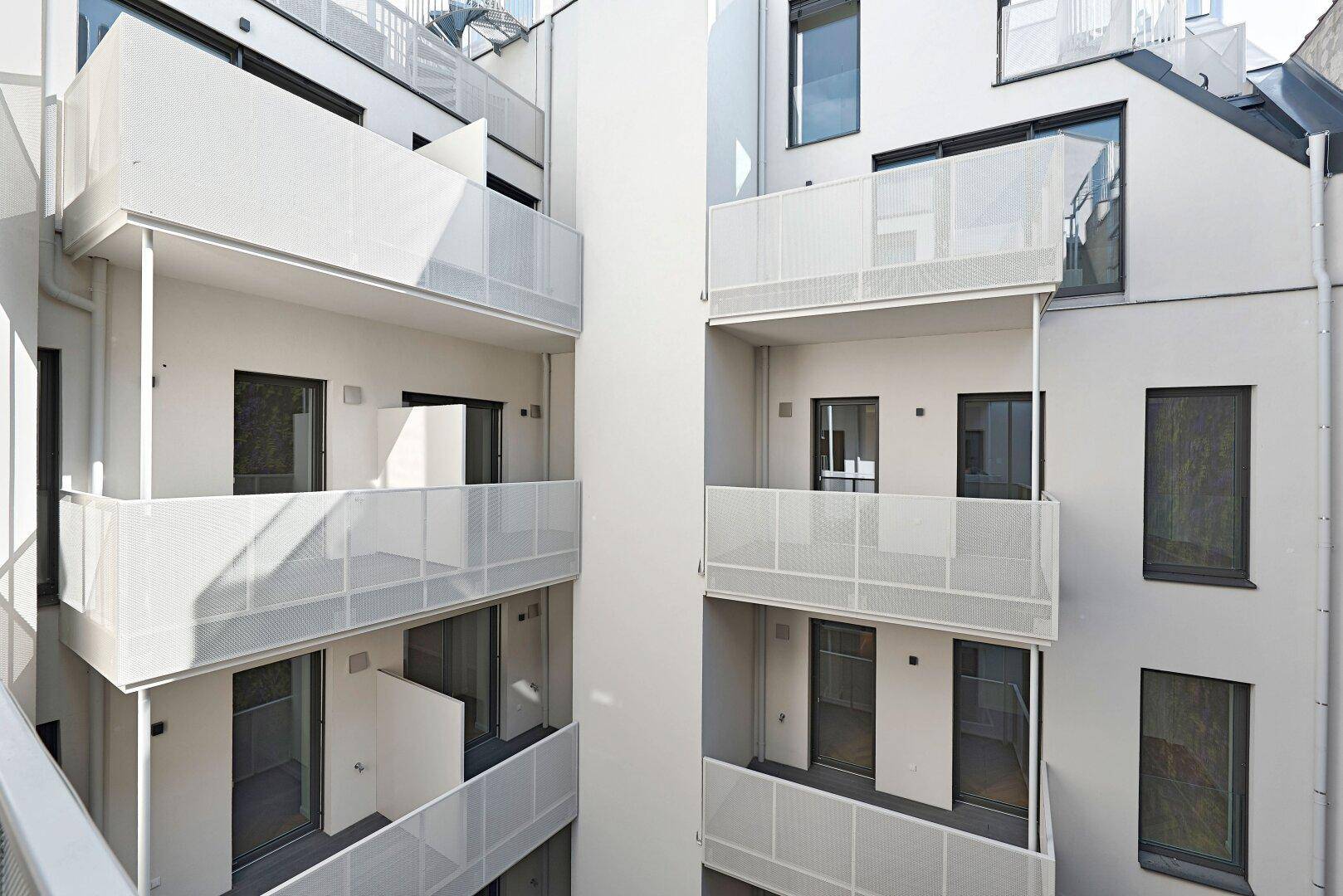 Ansicht mehrerer moderner Balkone und Fassaden in einem hellen Innenhof, mit viel Tageslicht.