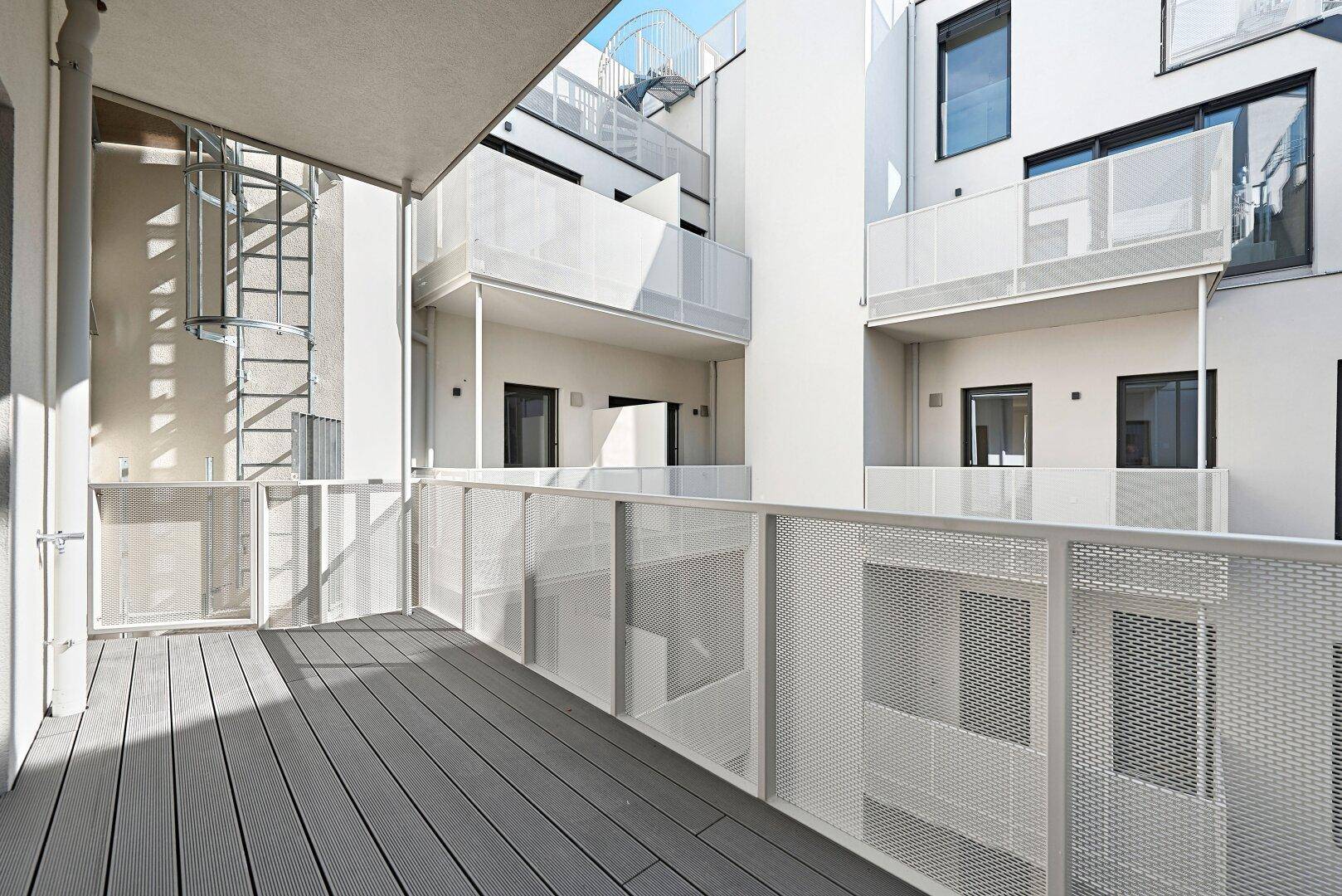 Moderne Balkone mit Metallgeländern in einem hellen Innenhofbereich, bieten zusätzlichen Wohnraum.