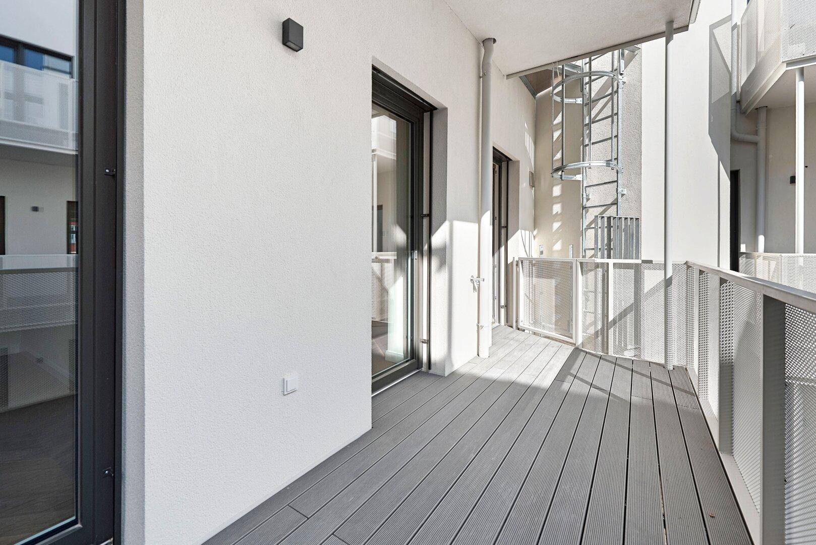 Moderner Balkon mit grauem Bodenbelag und Metallgeländer in einem ruhigen Innenhofbereich.