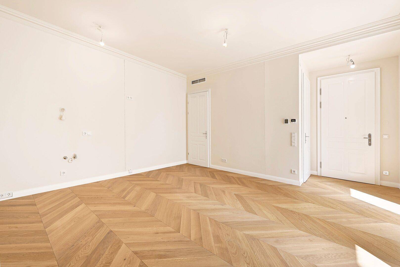 Geräumiges, helles Zimmer mit elegantem Fischgrätparkett und weißen Wänden, bereit zur individuellen Gestaltung.
