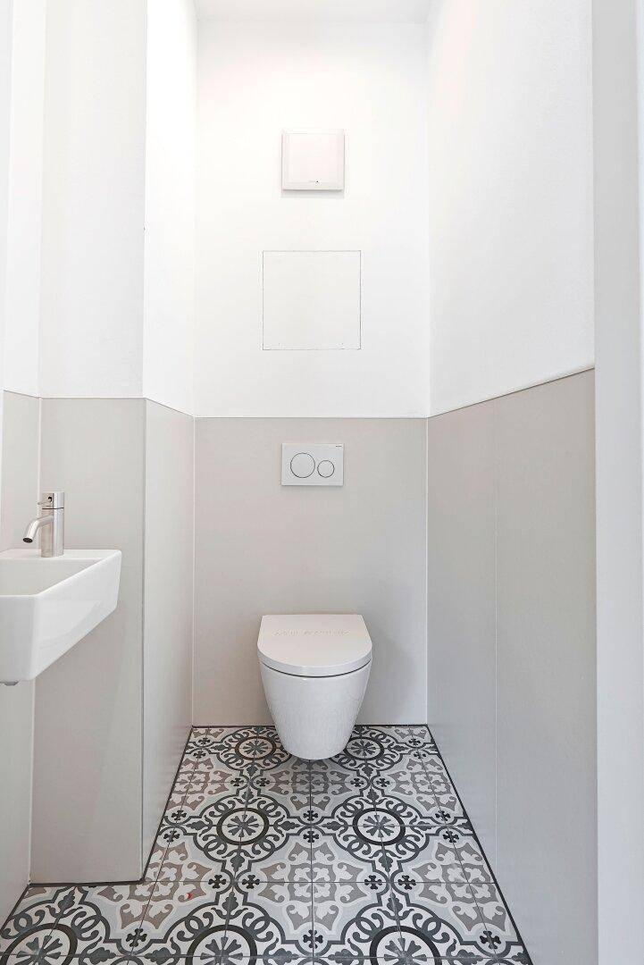 Modernes Gäste-WC mit gemusterten Fliesen, wandhängendem WC und kleinem Waschbecken.