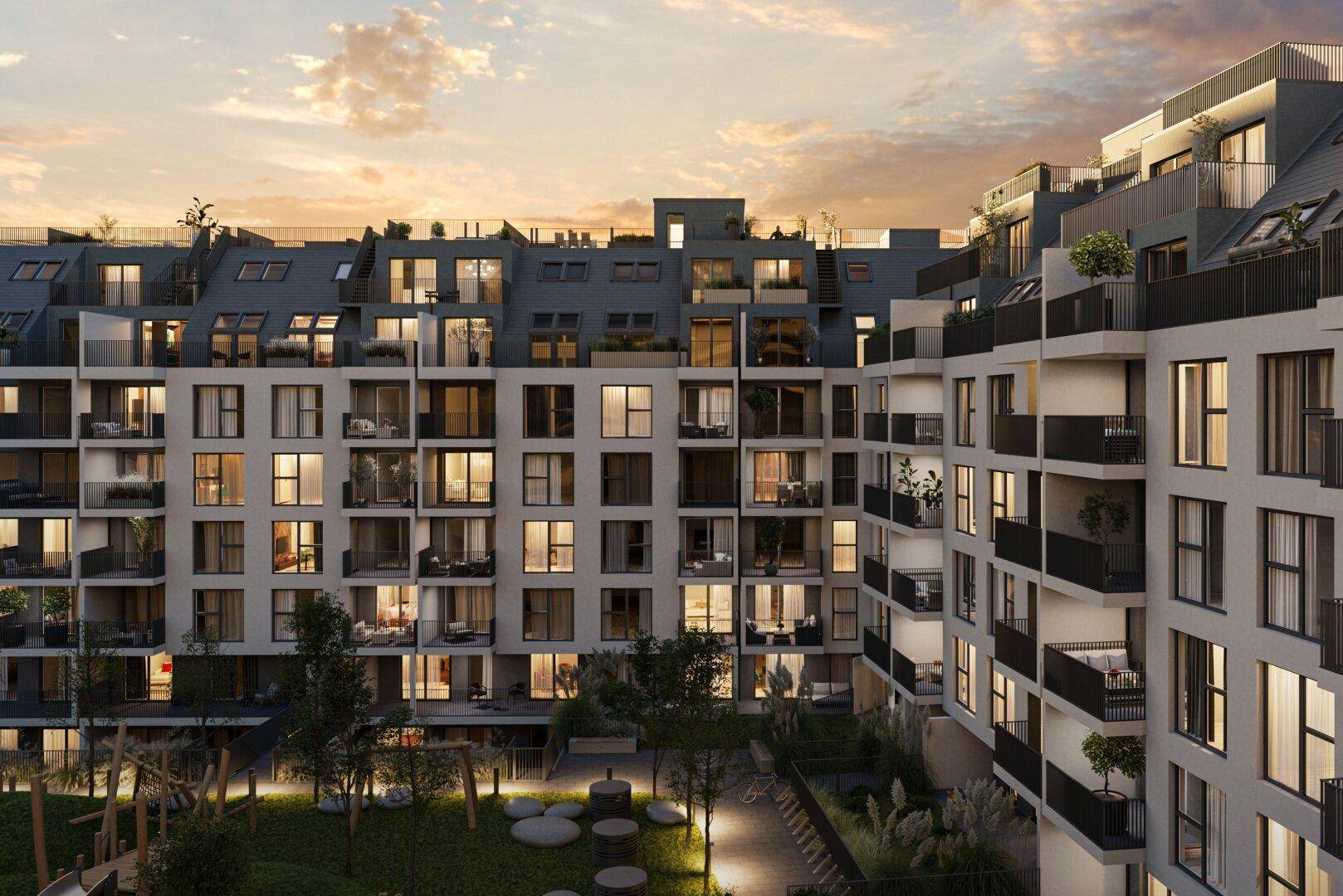 Moderne Wohnanlage bei Sonnenuntergang mit beleuchteten Balkonen und begrüntem Innenhof.