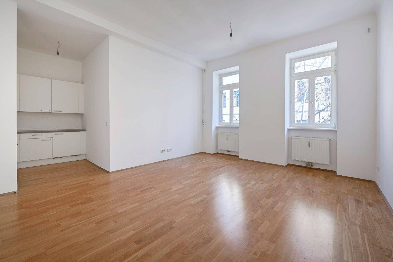 Heller Wohn- und Essbereich mit Parkettboden und integrierter Küchenzeile, ideal für offenes Wohnen.