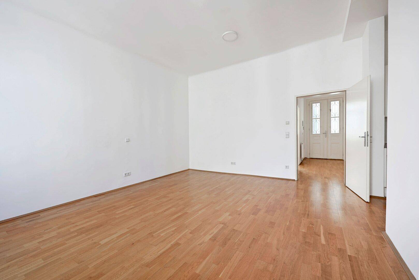 Geräumiger Raum mit Parkettboden und Zugang zu weiteren Zimmern durch elegante Doppeltüren.