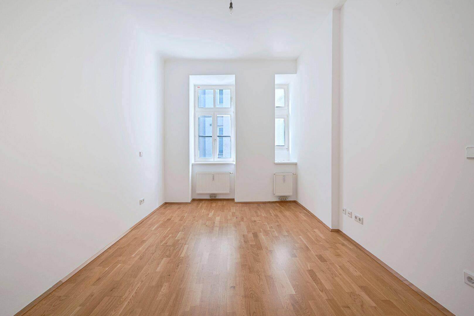 Langer, heller Raum mit Parkettboden und zwei Fenstern, bietet viel Platz für individuelle Einrichtungsideen.