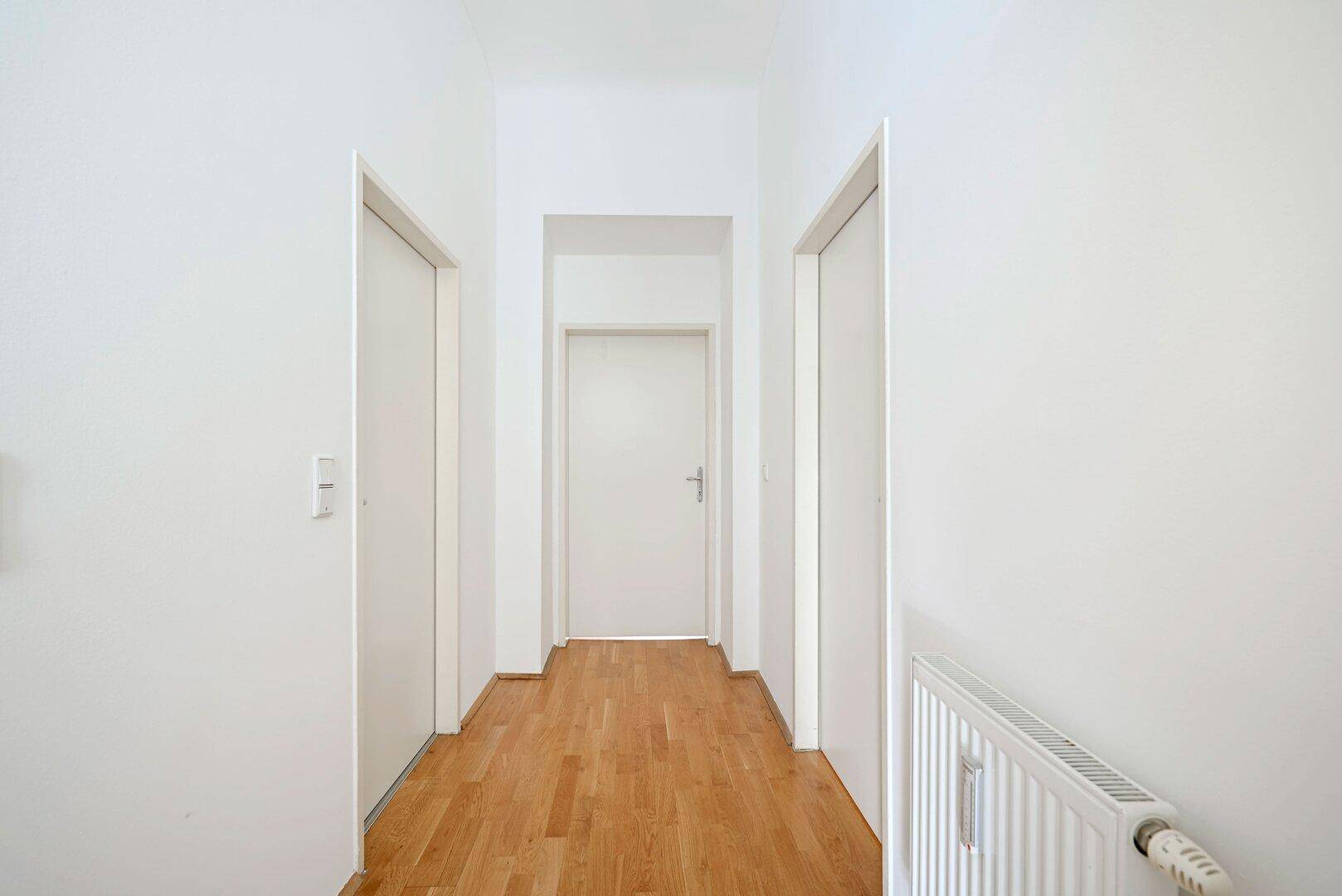 Schmaler Flur mit Parkettboden und mehreren Türen, führt zu den verschiedenen Zimmern der Wohnung.