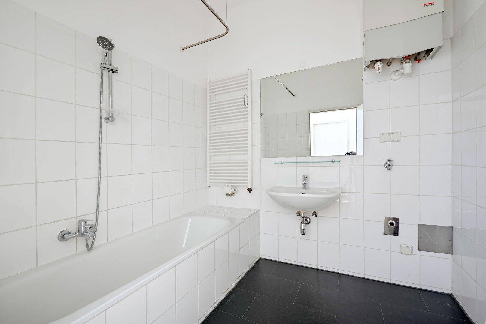 Modernes Badezimmer mit Badewanne, Dusche, Waschbecken und beheiztem Handtuchhalter, hell gefliest.
