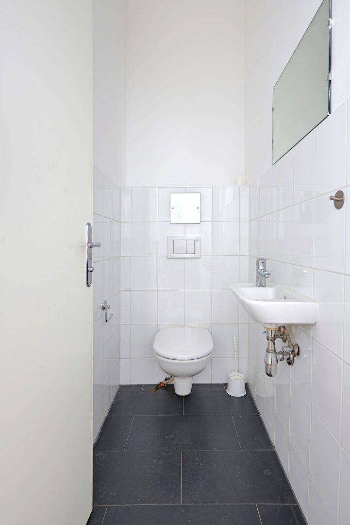 Separates WC mit wandhängender Toilette und kleinem Waschbecken, komplett weiß gefliest.