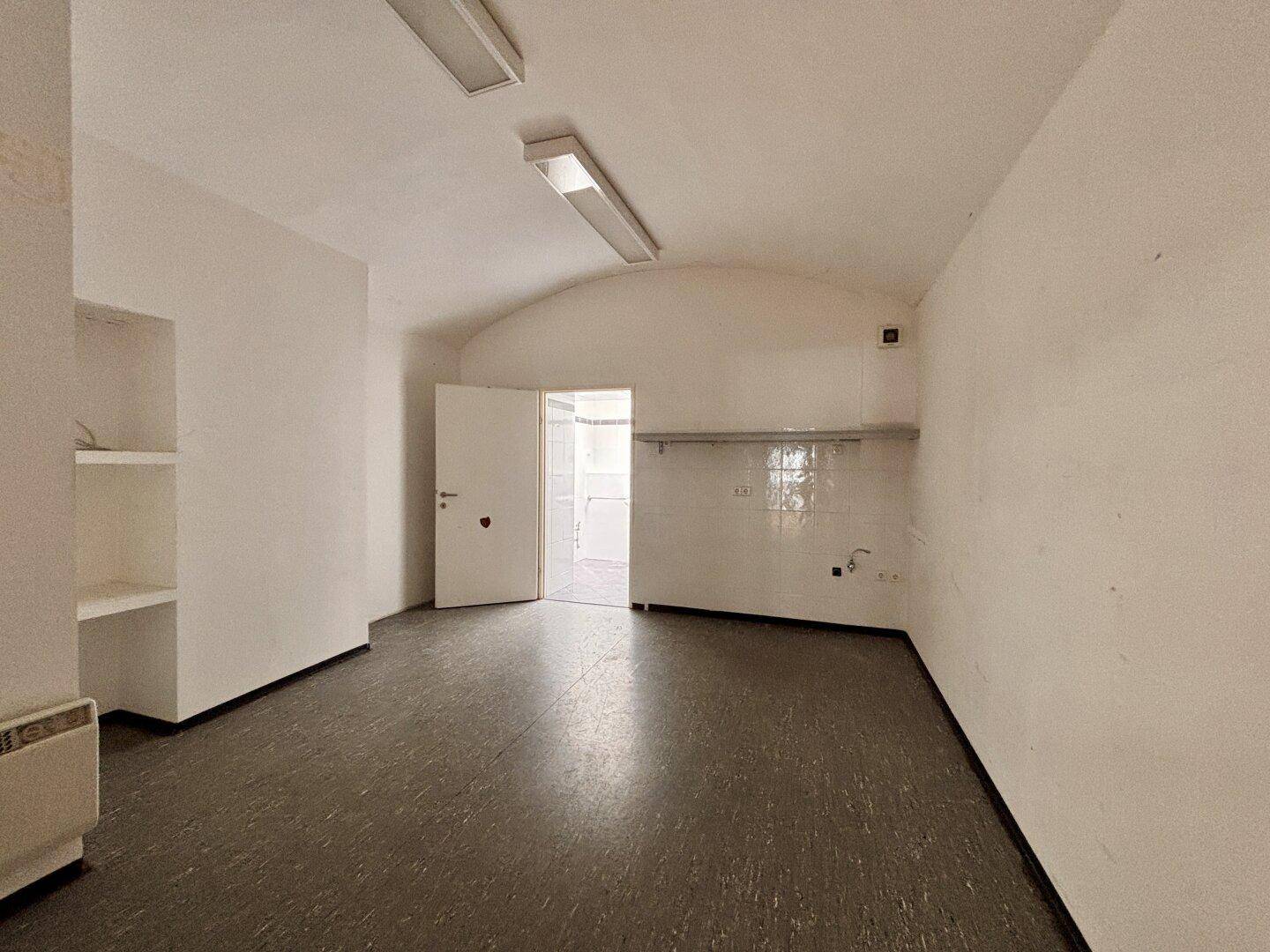 Kleinerer Raum mit dunklem Boden, weißen Wänden und Gewölbedecke, möglicherweise ein Lager oder Nebenraum.