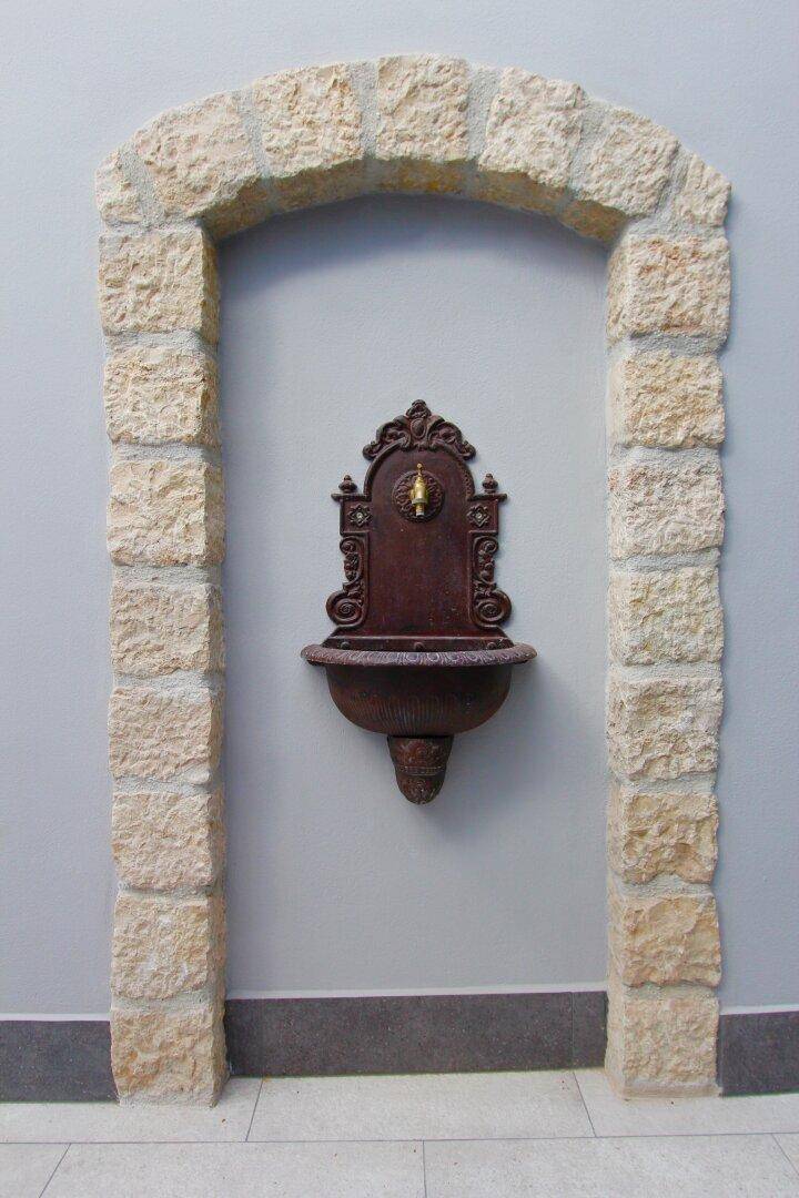 Dekorative Wandnische mit Steinrahmen und einem antiken Wandbrunnen in einem Innenbereich.
