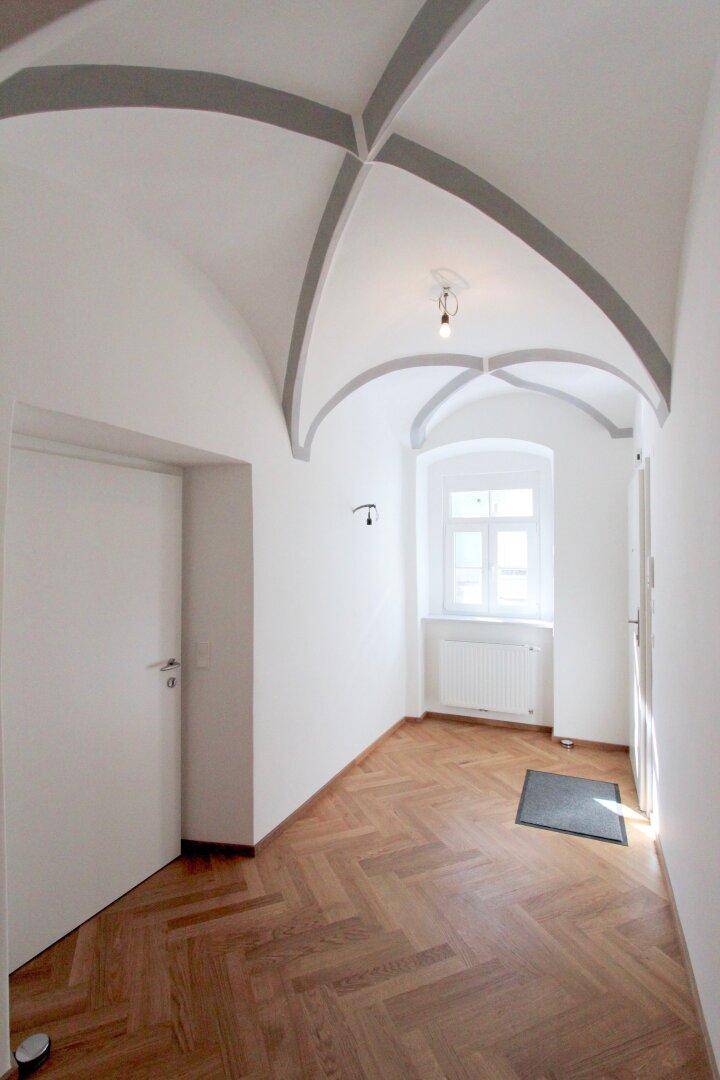 Heller Flur mit Fischgrätparkett, einem Fenster und einem eleganten Gewölbedecke.