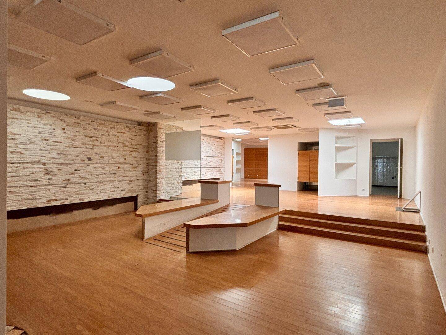 Großer offener Raum mit Holzfußboden, einer Steinwand und modernen Deckenleuchten.