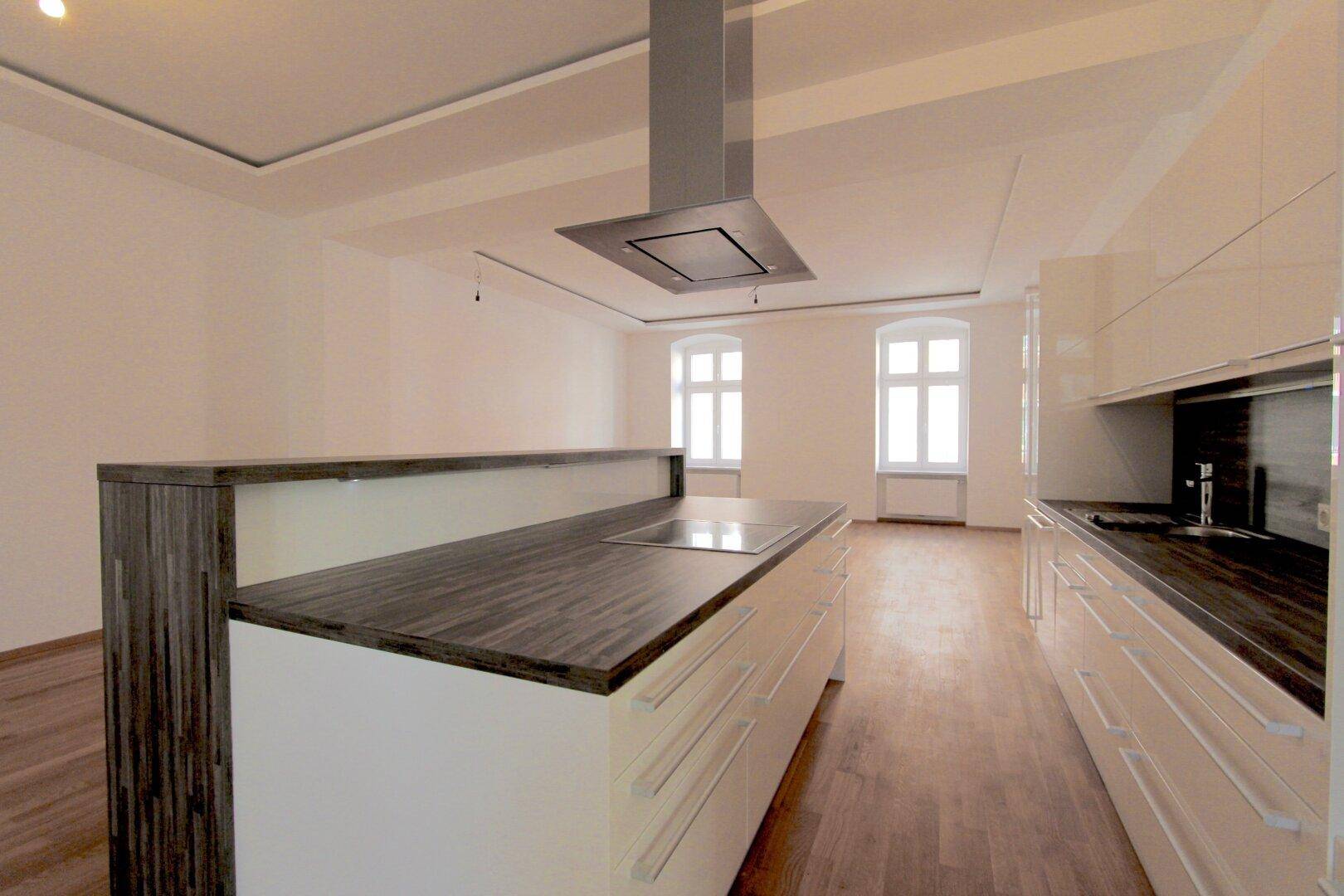 Moderne offene Küche mit Kochinsel, Dunstabzugshaube und Holzboden in einem hellen Raum.