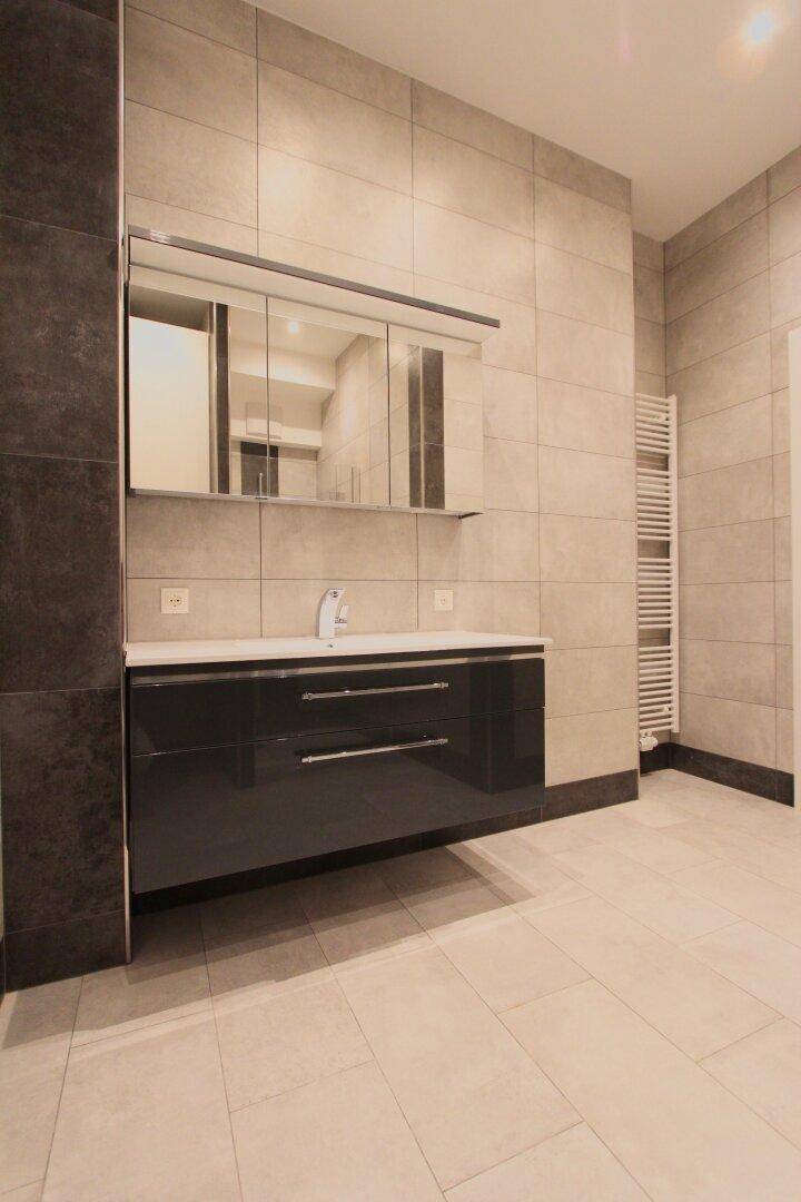 Modernes Badezimmer mit großformatigen Fliesen, schwebendem Waschtisch und beheiztem Handtuchhalter.
