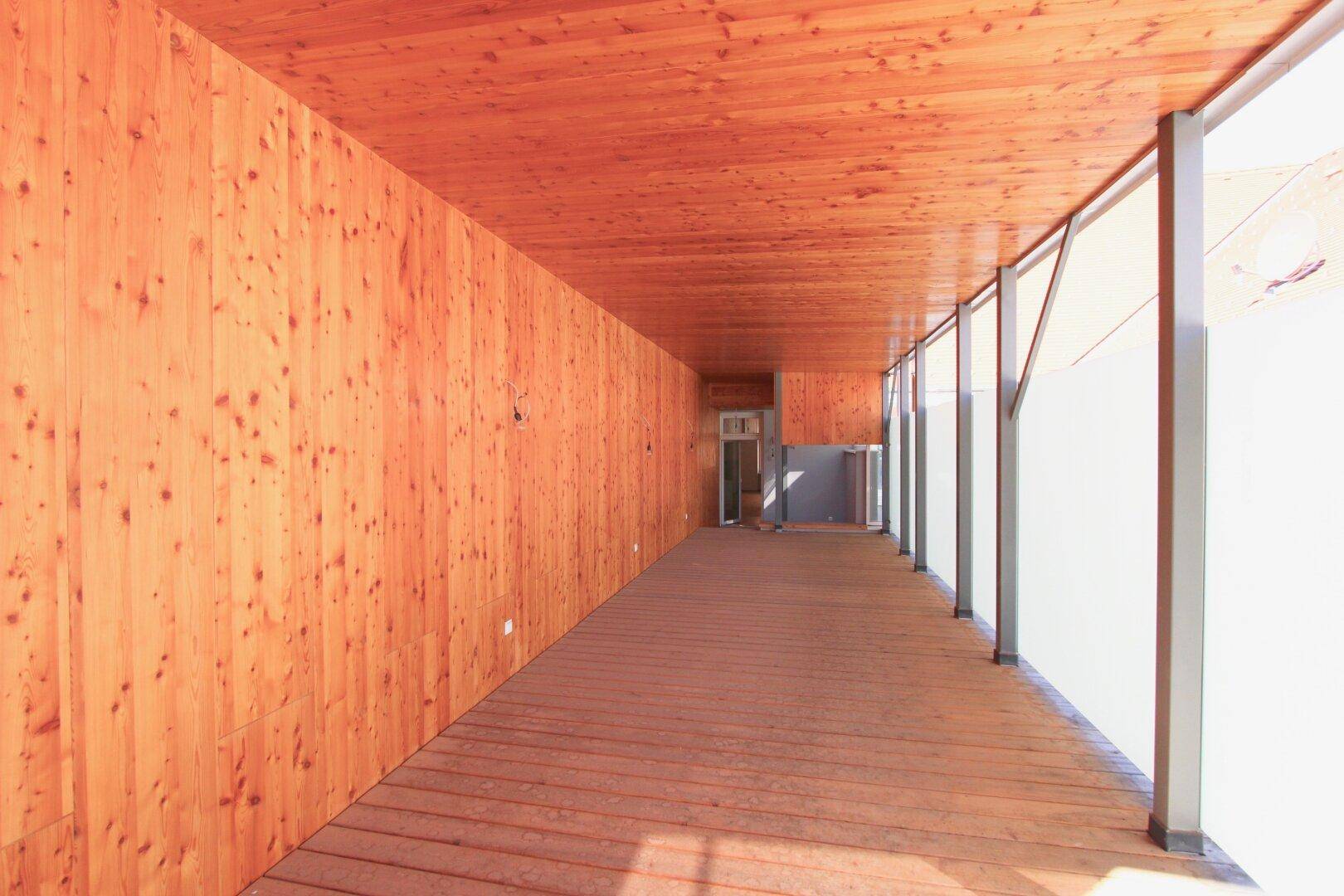 Langer, holzverkleideter Gang mit großen Fenstern, die viel Tageslicht hereinlassen.