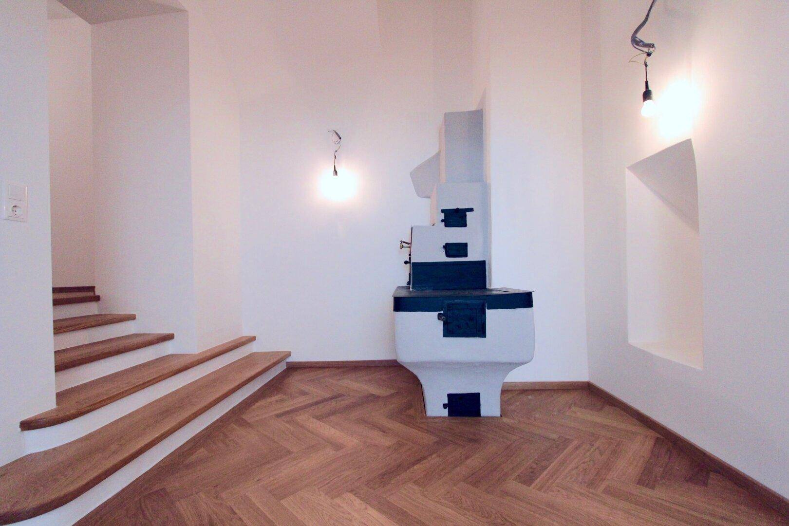 Bereich mit Fischgrätparkett, einer Holztreppe und einem traditionellen Kachelofen als Heizelement.