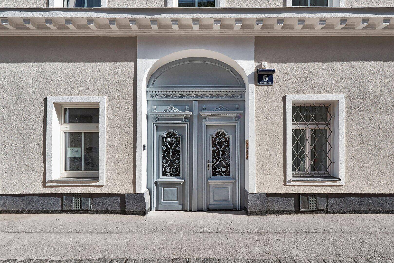 Detailansicht des Haupteingangs eines Altbaus mit kunstvoll verzierten Doppeltüren und Fenstergittern.