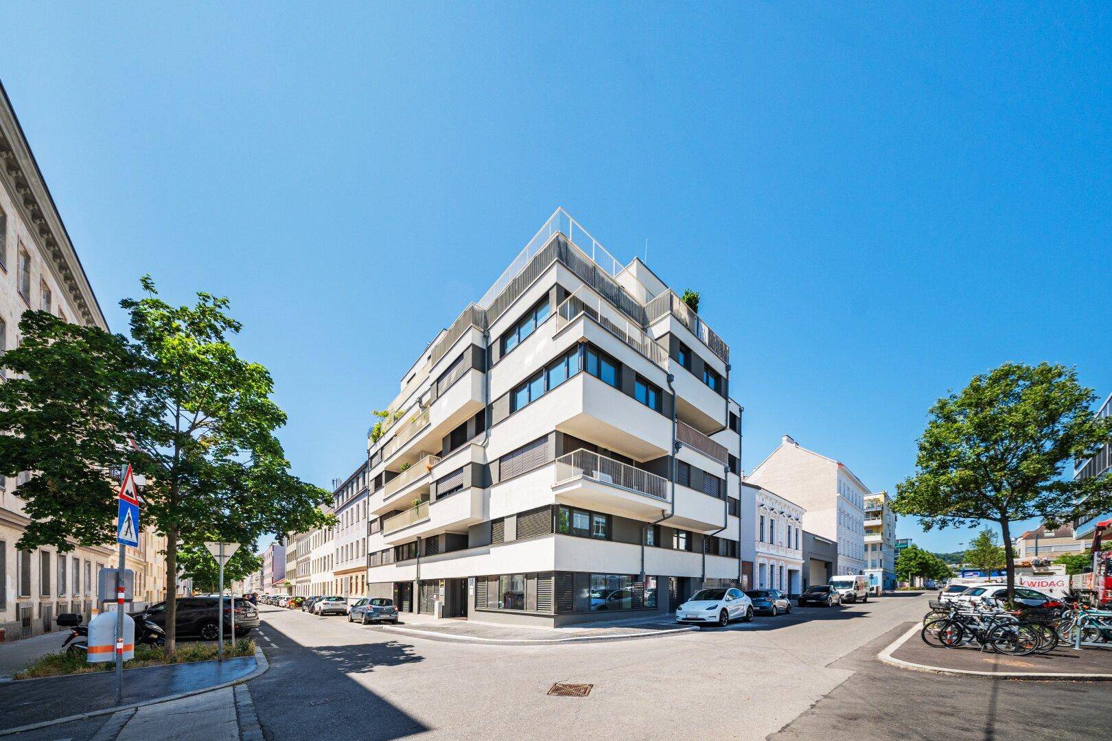 Modernes Eckgebäude mit Balkonen und großen Fenstern an einer belebten Straße.