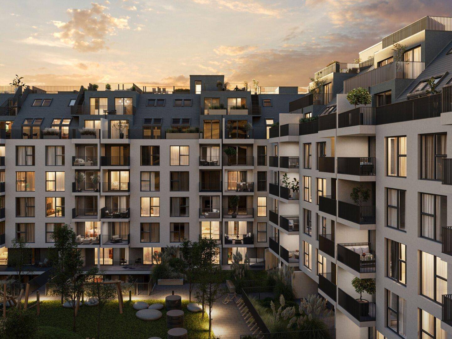 Moderne Wohnanlage mit zahlreichen Balkonen, Dachterrassen und einem begrünten Innenhof bei Sonnenuntergang.