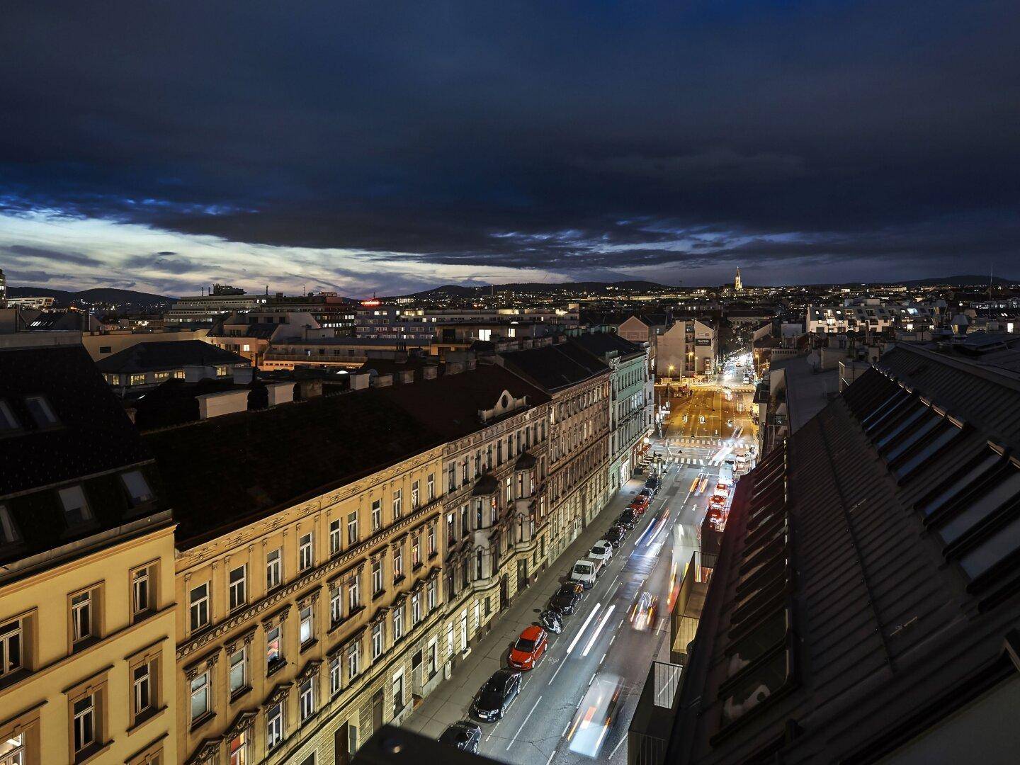 Panoramablick über die beleuchtete Stadt bei Nacht mit langen Lichtspuren der Fahrzeuge.