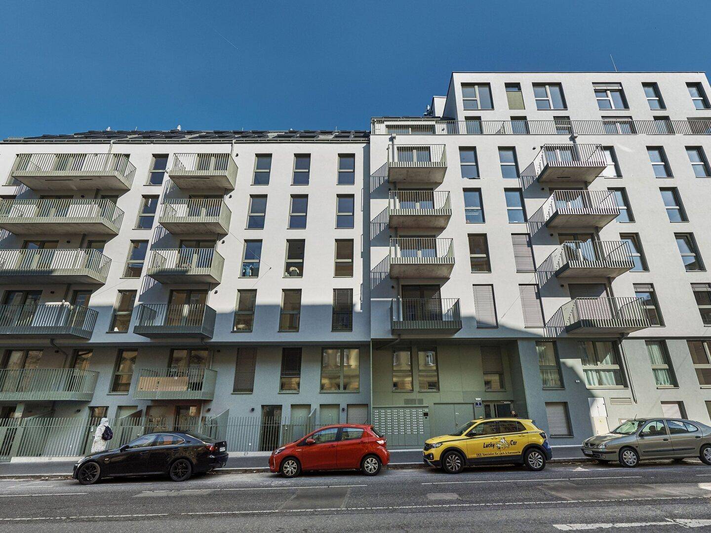 Moderne Wohngebäude-Fassade mit zahlreichen Balkonen und geparkten Autos entlang der Straße.