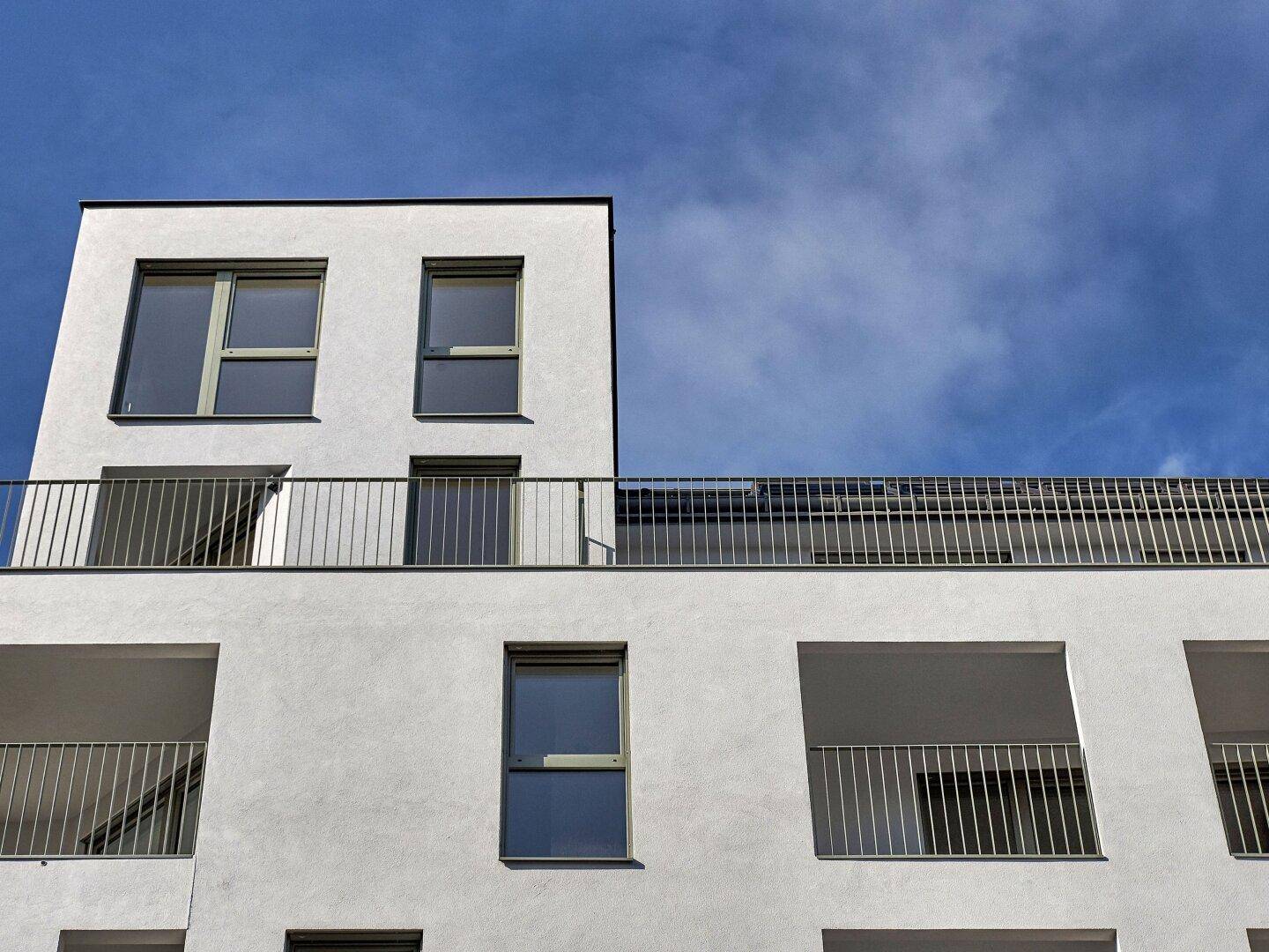 Oberer Teil des modernen Gebäudes mit einer Dachterrasse und klarem blauem Himmel.