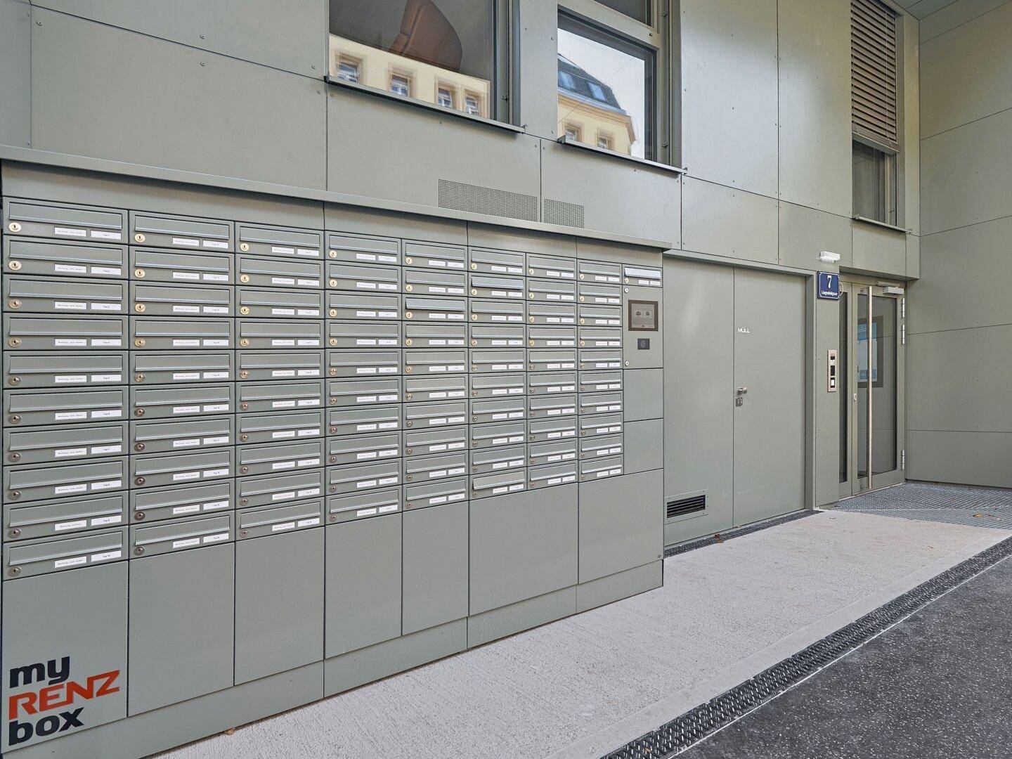 Eingangsbereich des Gebäudes mit einer großen Ansammlung moderner Briefkästen und Paketboxen.