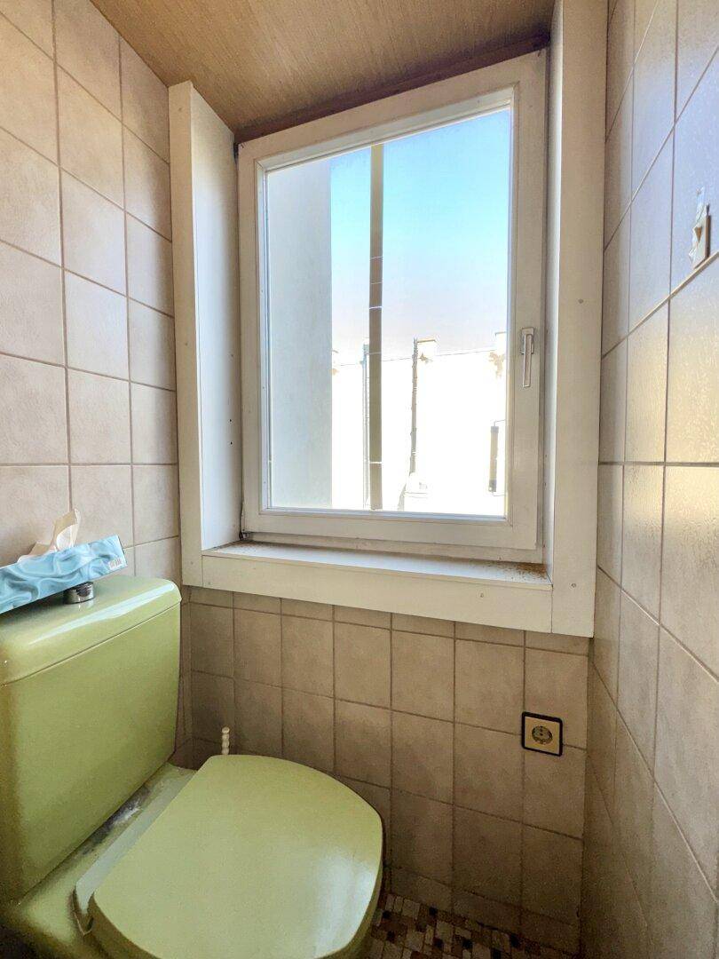 Kleines WC mit grünem WC-Becken, Fliesen an den Wänden und einem Fenster für Tageslicht.