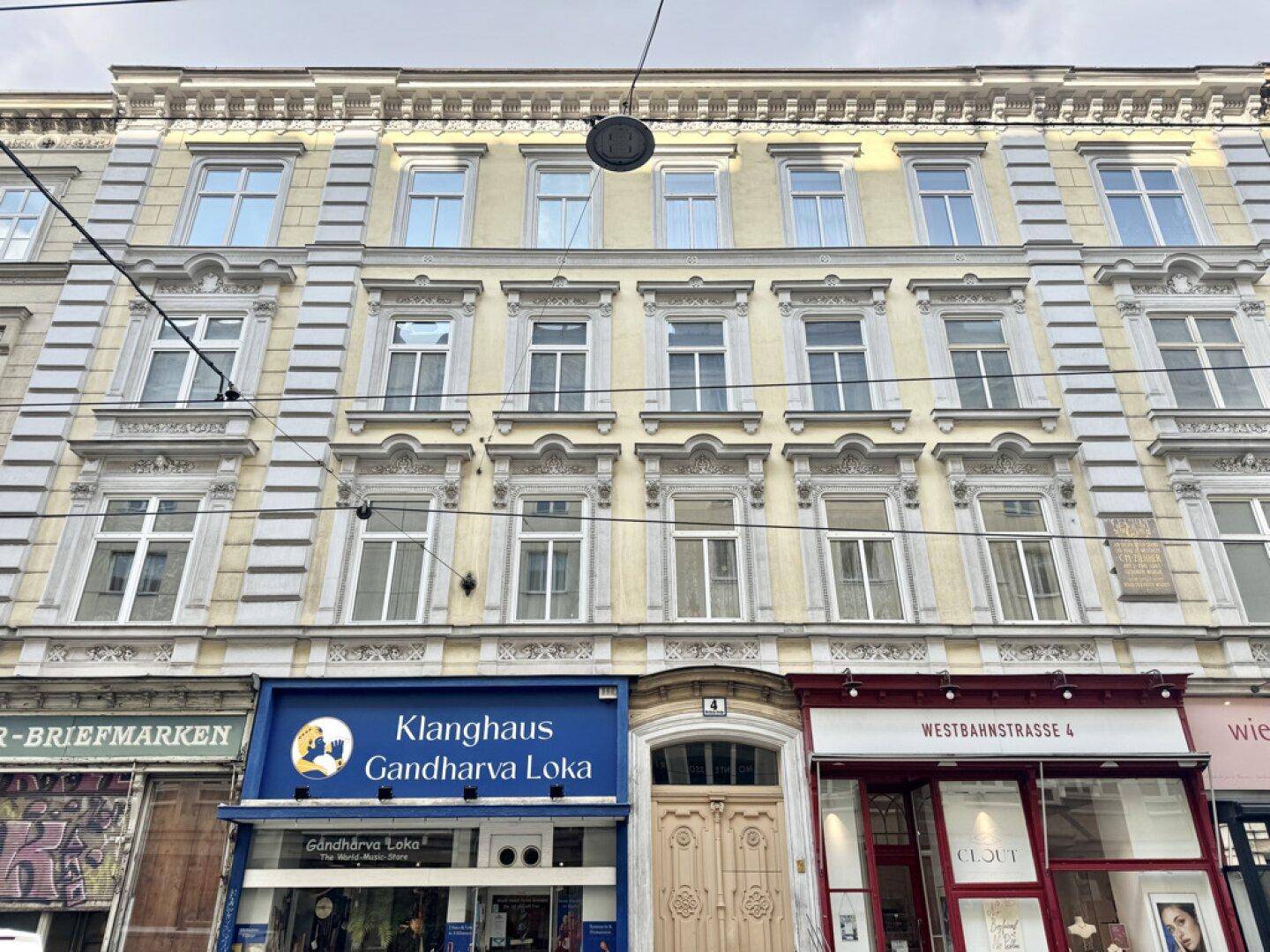 Historische Fassade eines Mehrfamilienhauses mit reich verzierten Fenstern und Geschäften im Erdgeschoss.