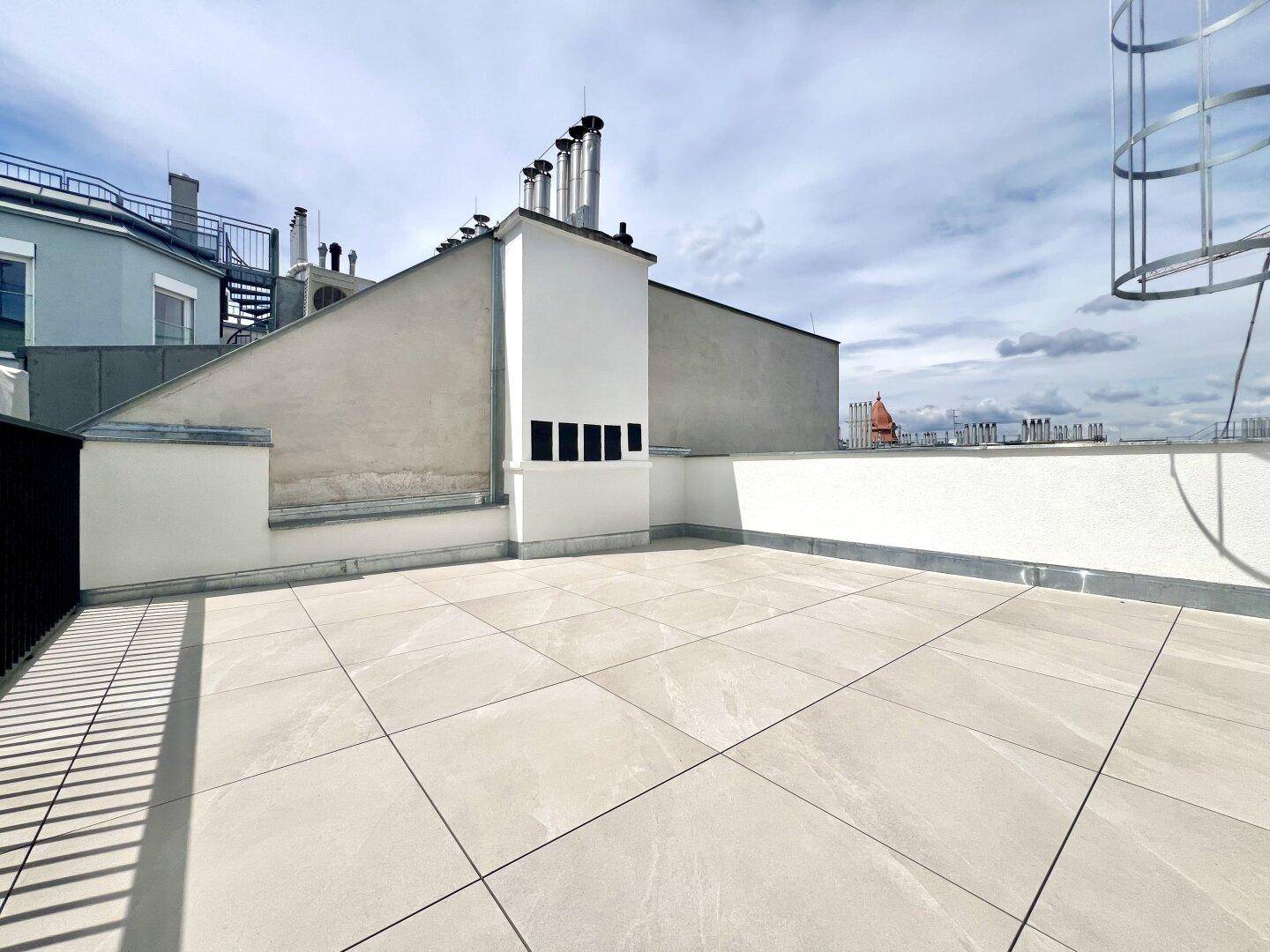 Geräumige Dachterrasse mit hellen Fliesen und Blick auf die umliegenden Dächer der Stadt.