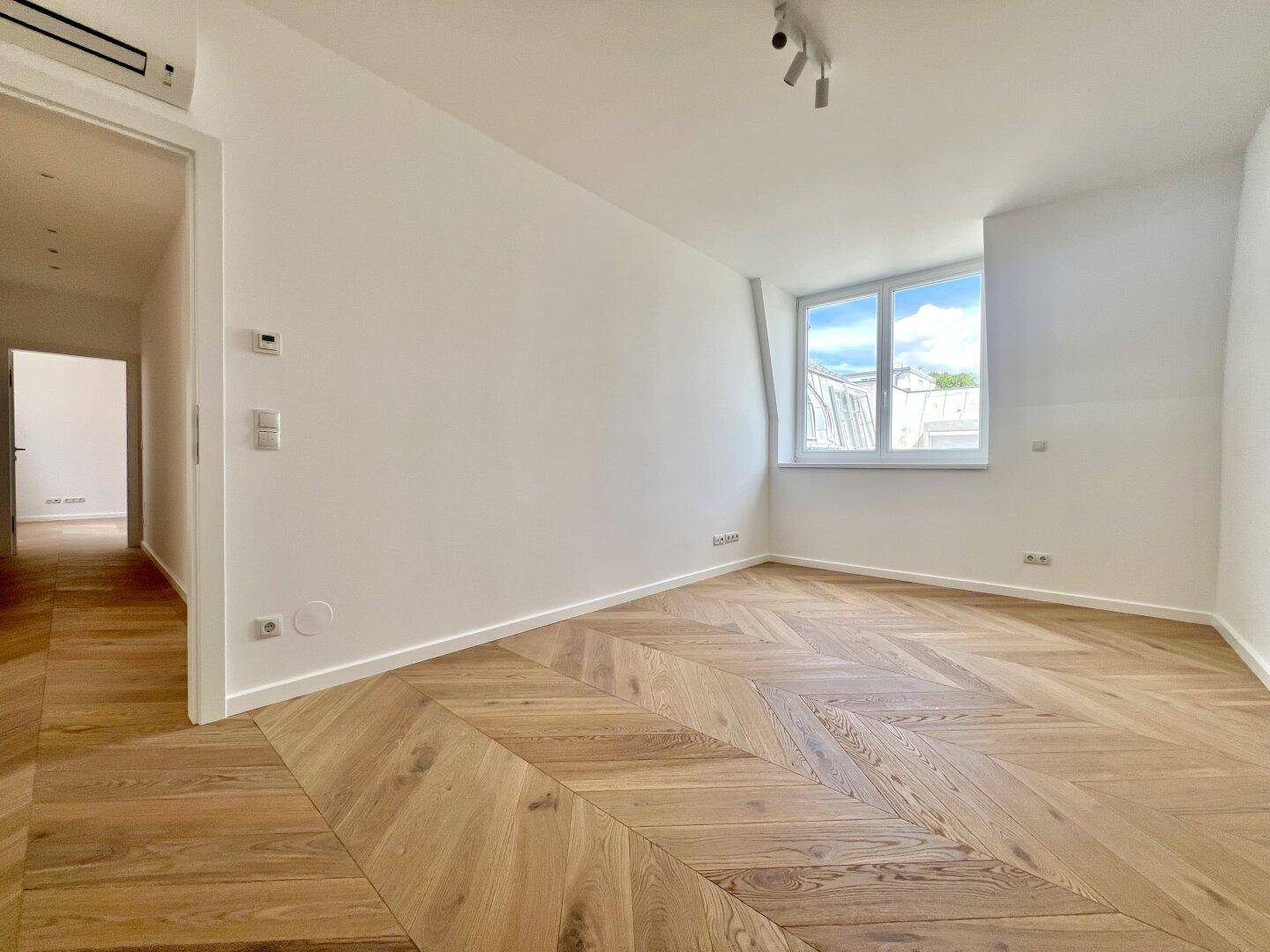 Helles Zimmer mit Fischgrätparkett, einem Fenster und moderner Ausstattung.