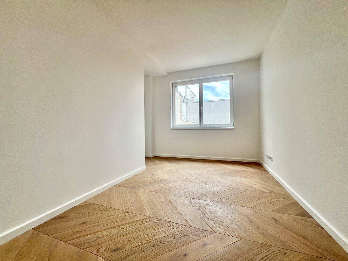 Kleines, helles Zimmer mit Fischgrätparkett und einem Fenster.