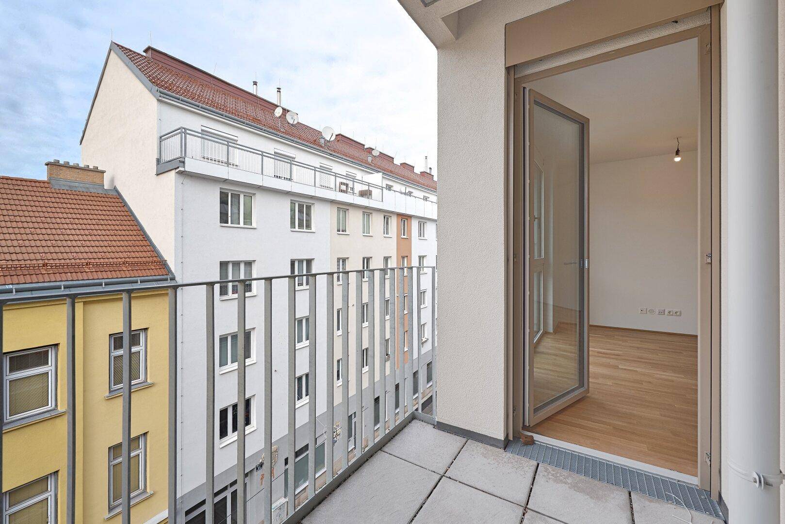 Geräumiger Balkon mit Fliesenboden und Blick auf die moderne Gebäudefassade.