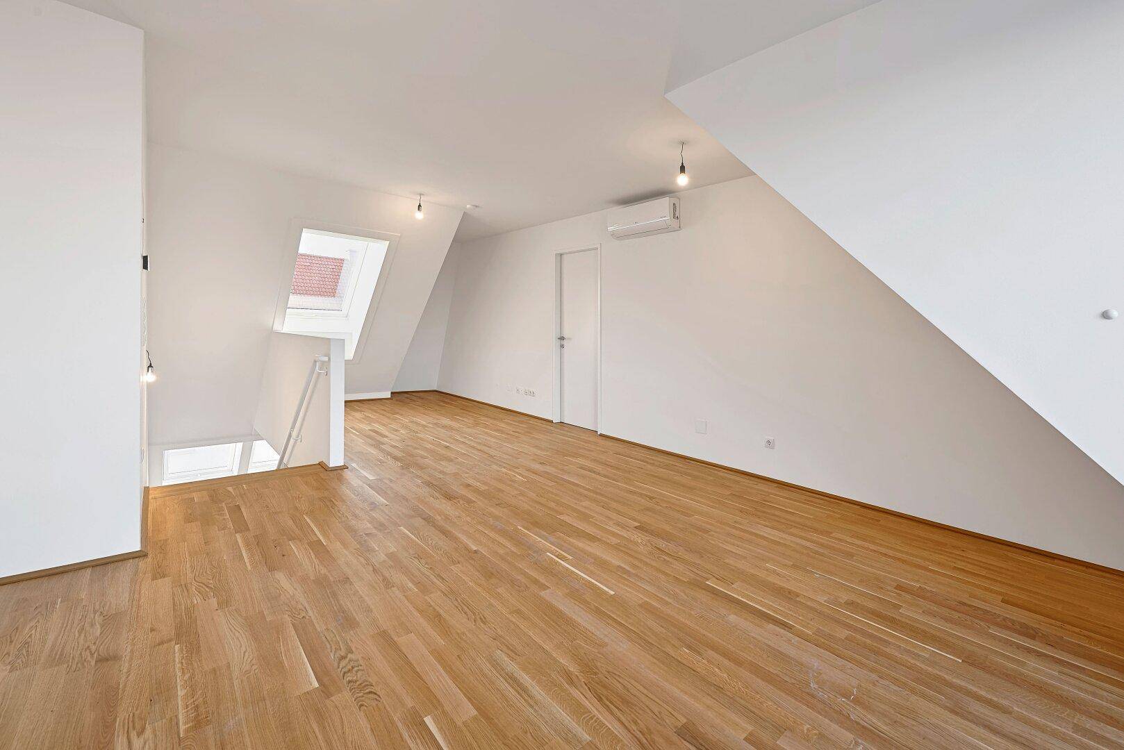 Leerer Dachgeschossraum mit Holzboden, Dachfenster und Klimaanlage, bereit zur individuellen Gestaltung.