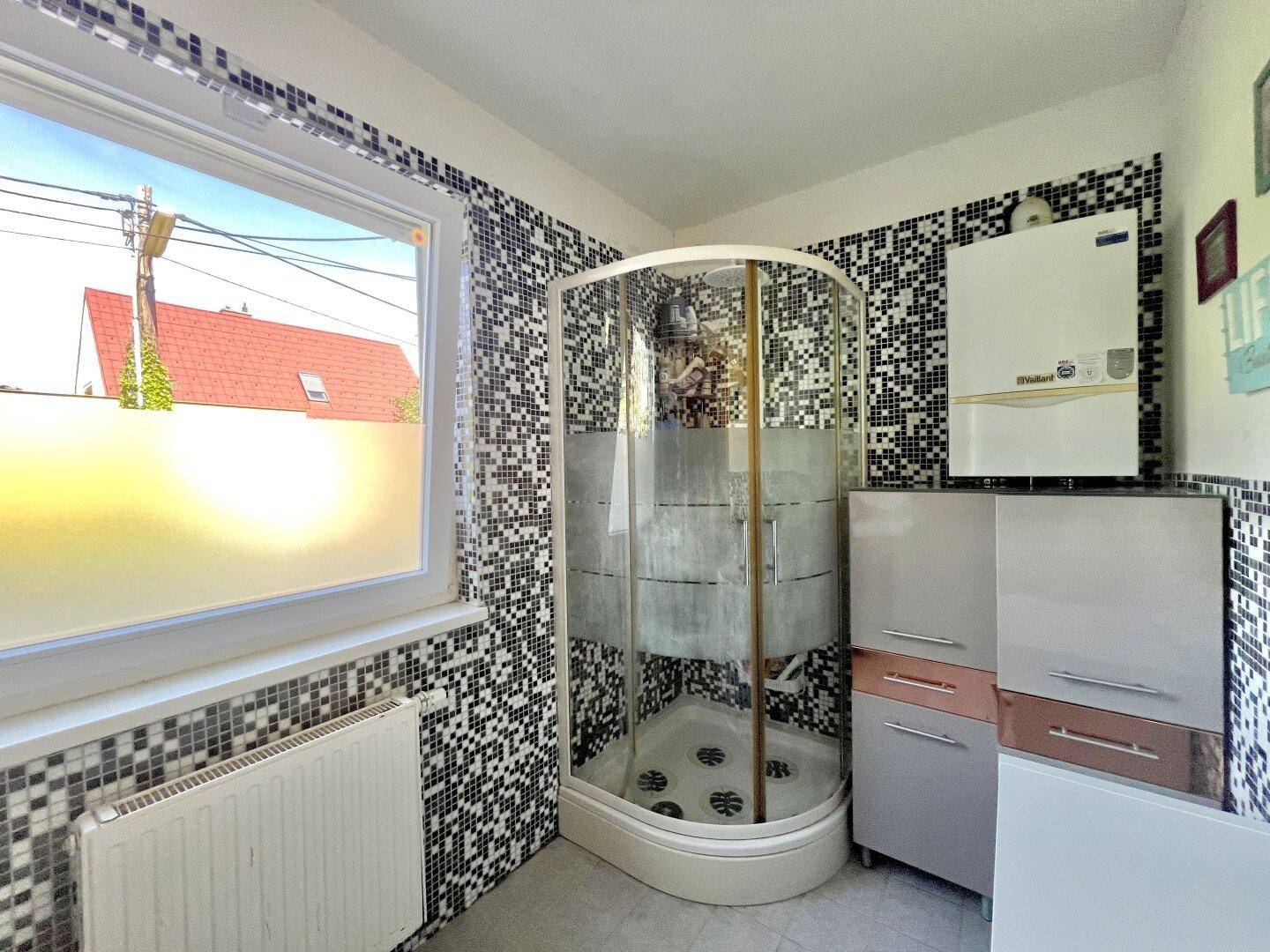 Badezimmer mit Duschkabine, schwarz-weißen Mosaikfliesen und Fenster.