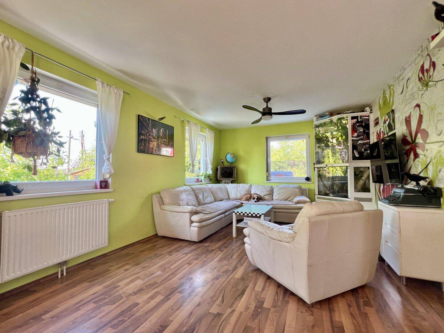 Gemütliches Wohnzimmer mit bequemer Eckcouch, Holzboden und hellgrünen Wänden.