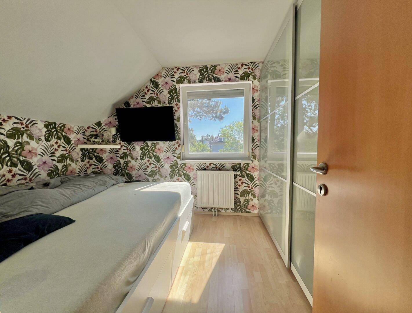 Schlafzimmer mit Dachschräge, floraler Tapete und integriertem Kleiderschrank.