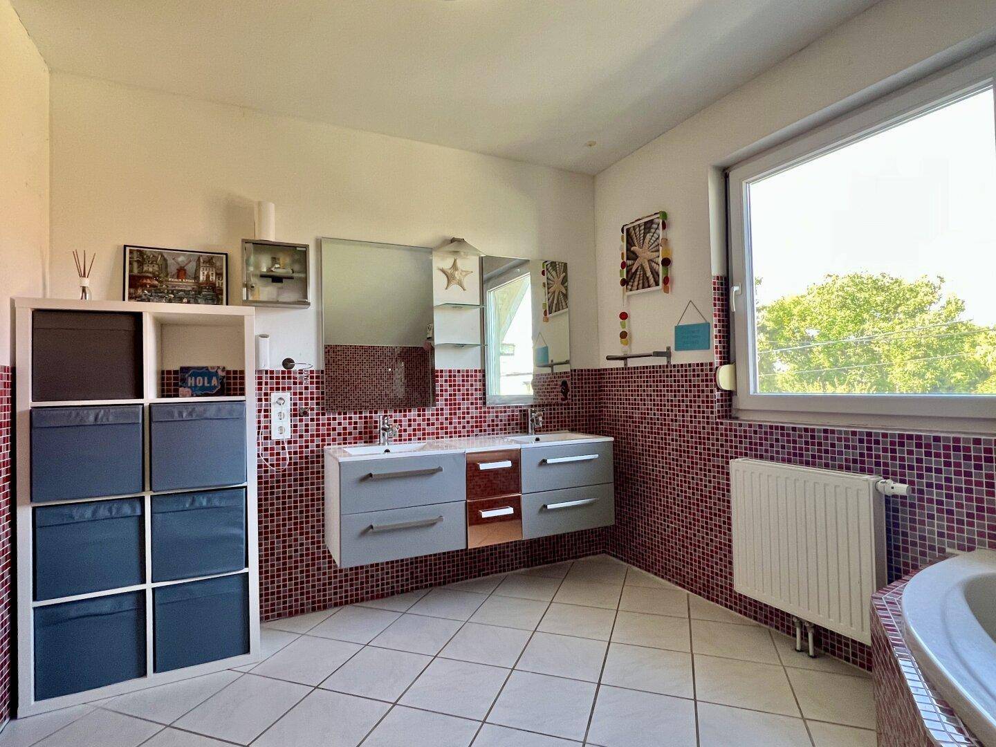 Geräumiges Badezimmer mit Doppelwaschbecken, roten Mosaikfliesen und Fenster.