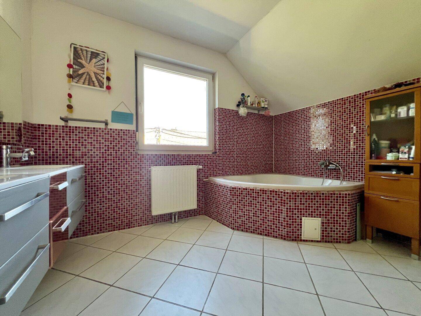 Badezimmer mit Eckbadewanne, roten Mosaikfliesen und Fenster unter der Dachschräge.