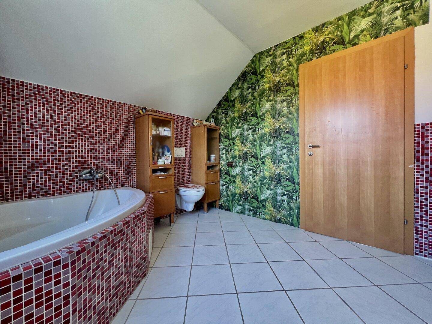 Badezimmer mit Badewanne, WC und auffälliger tropischer Tapete an einer Wand.
