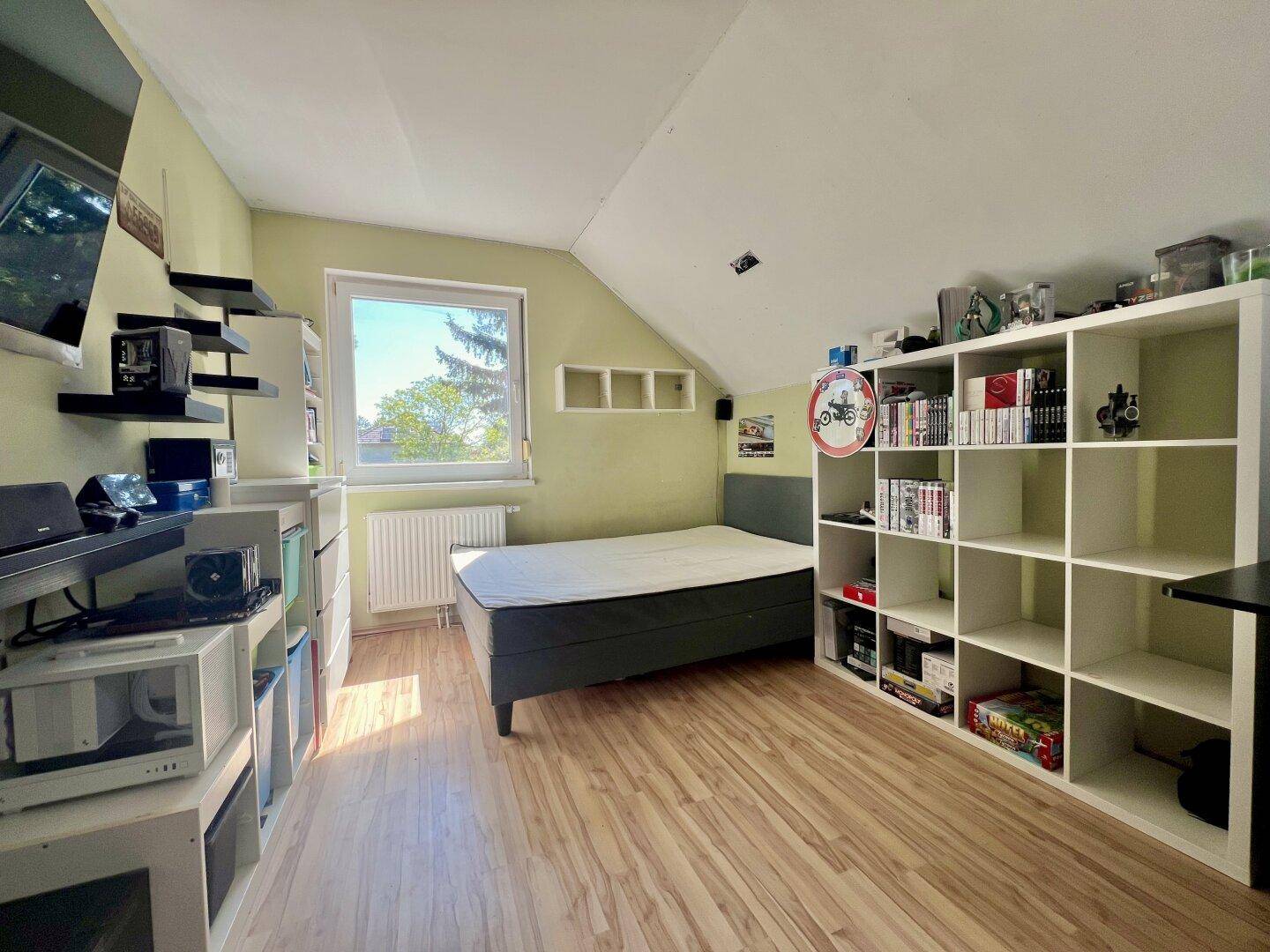 Helles Schlafzimmer mit Holzboden, Dachschräge und Regalsystem für Stauraum.