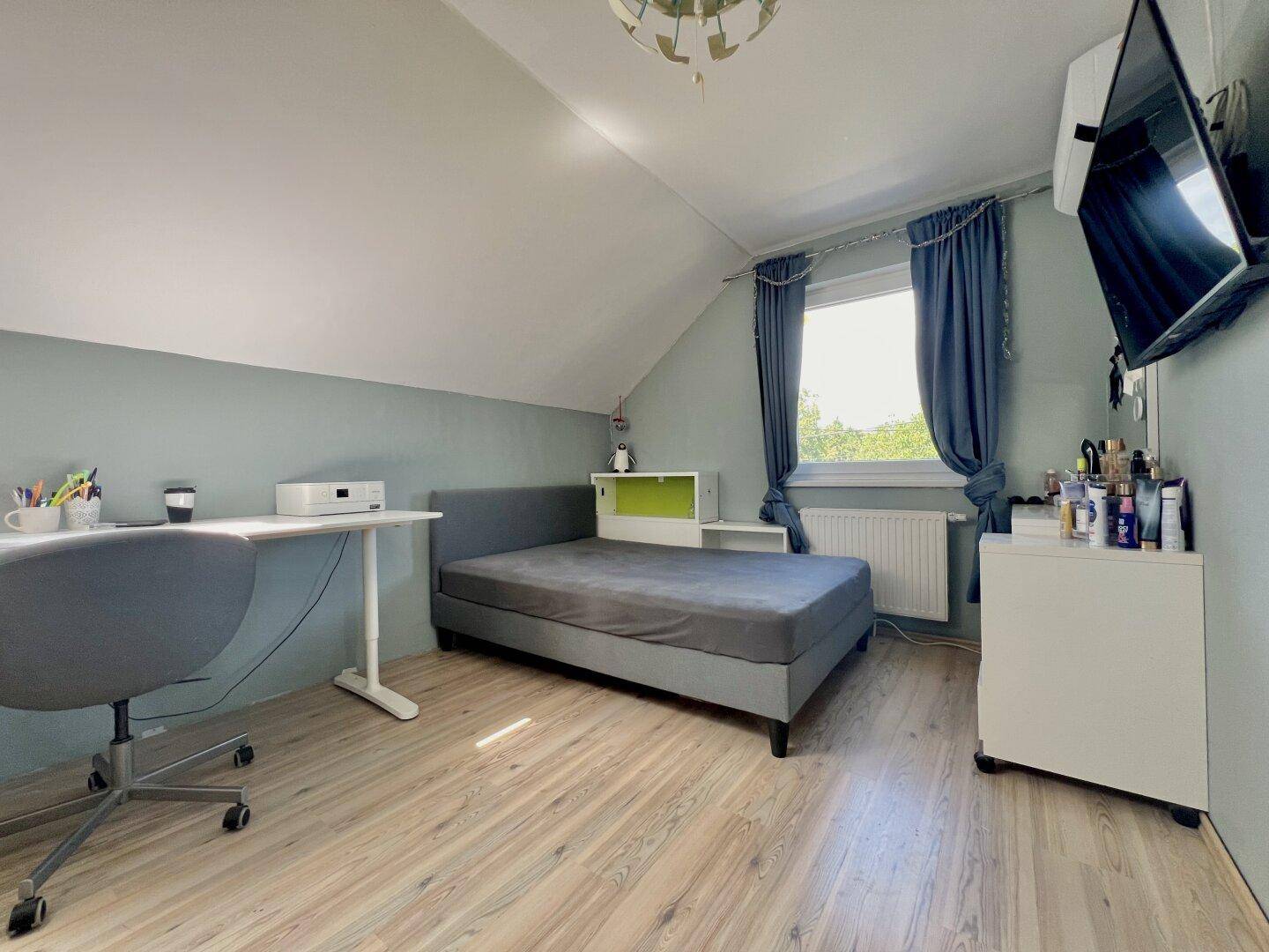 Jugendzimmer mit Schreibtisch, Bett und Dachschräge, hell und funktional eingerichtet.