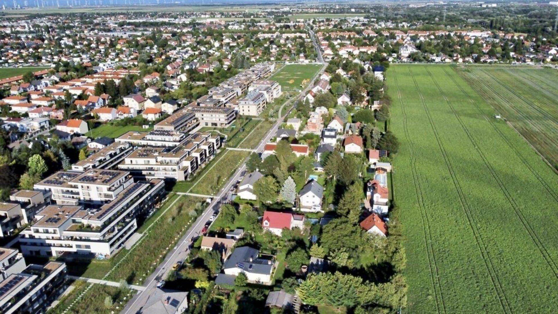 Weitläufige Luftaufnahme eines Wohngebiets mit neuen Gebäuden und Feldern am Horizont.