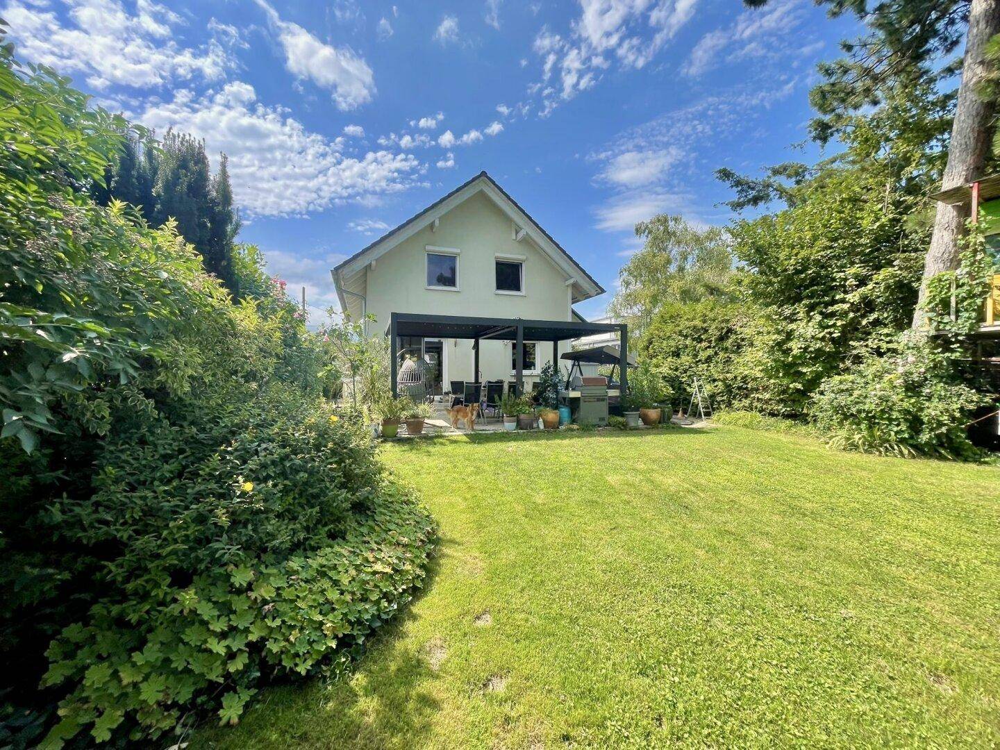 Weitläufiger Garten mit Rasenfläche und dem Haus im Hintergrund, umgeben von viel Grün.