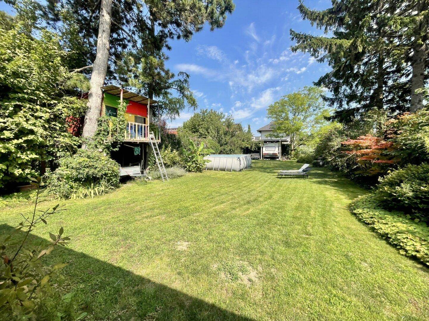 Weitläufiger Garten mit Rasenfläche, Aufstellpool und einem bunten Baumhaus für Kinder.