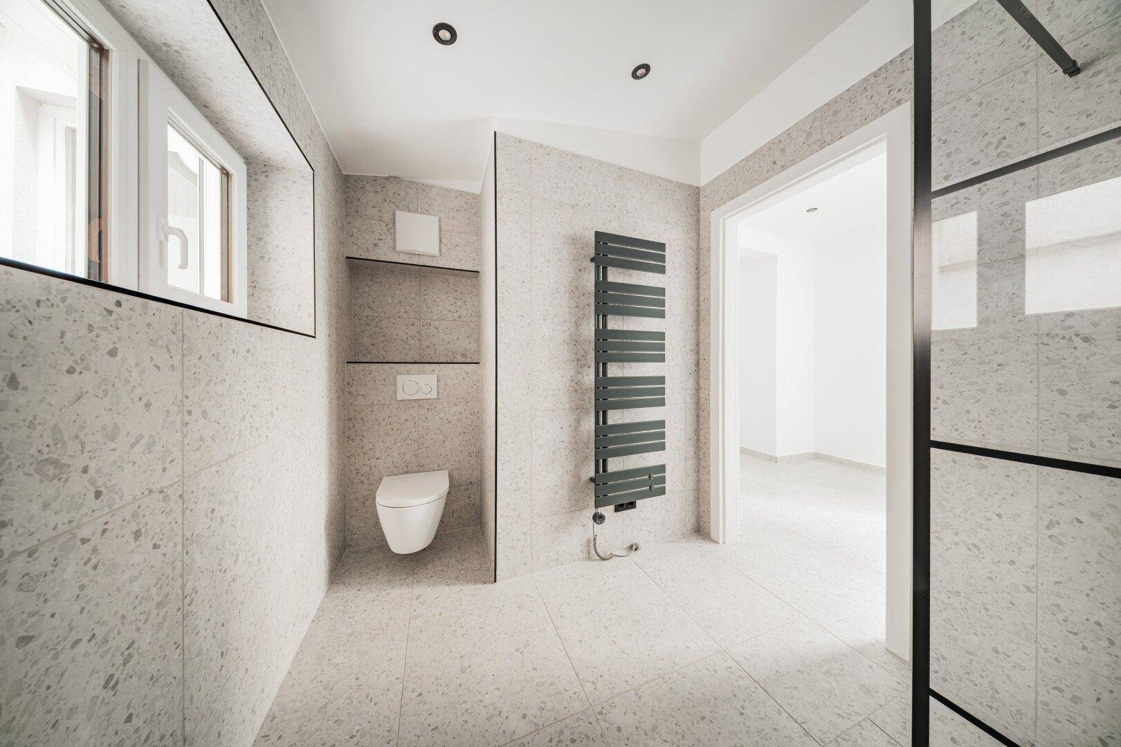 Modernes Badezimmer mit wandhängendem WC, Handtuchheizkörper und Fliesenboden.