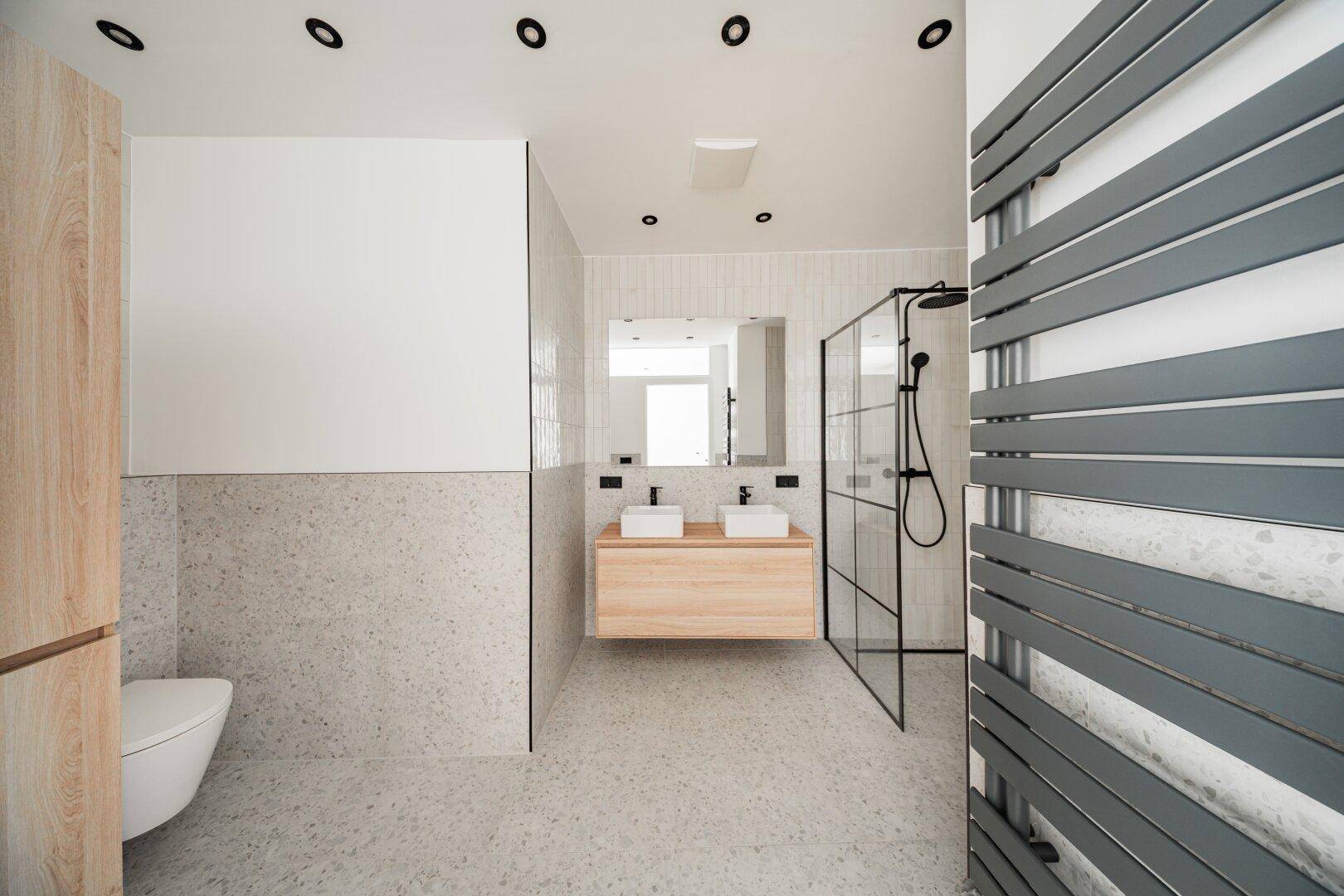 Modernes Badezimmer mit Doppelwaschbecken, wandhängendem WC und begehbarer Dusche.
