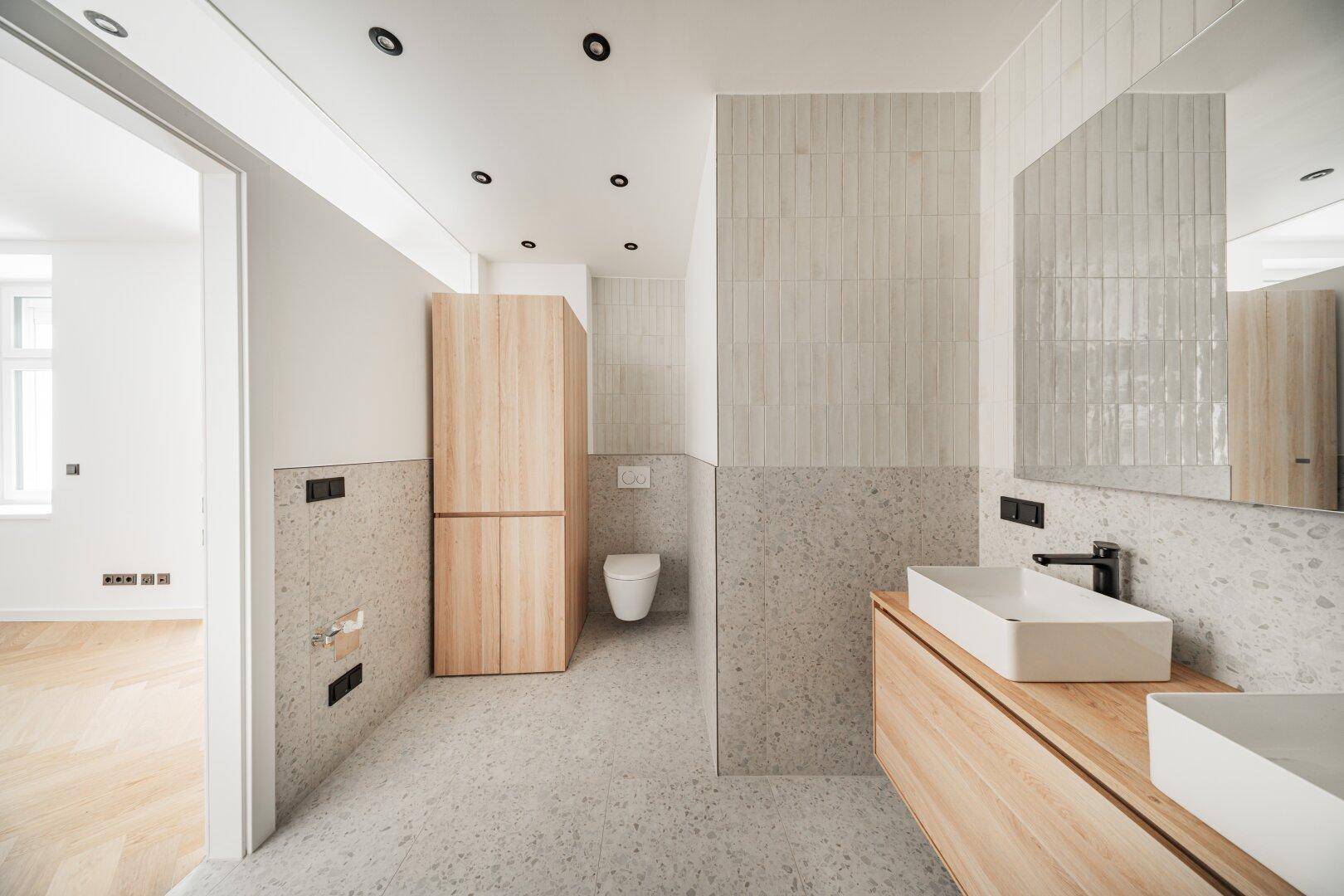 Modernes Badezimmer mit Doppelwaschbecken, Holzschränken und wandhängendem WC.