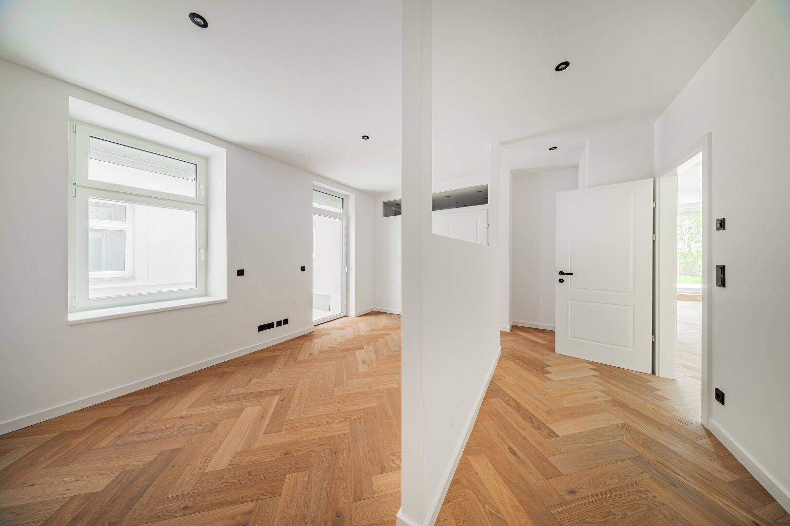 Heller Raum mit Fischgrätparkett und großen Fenstern, ideal als Wohn- oder Schlafzimmer.