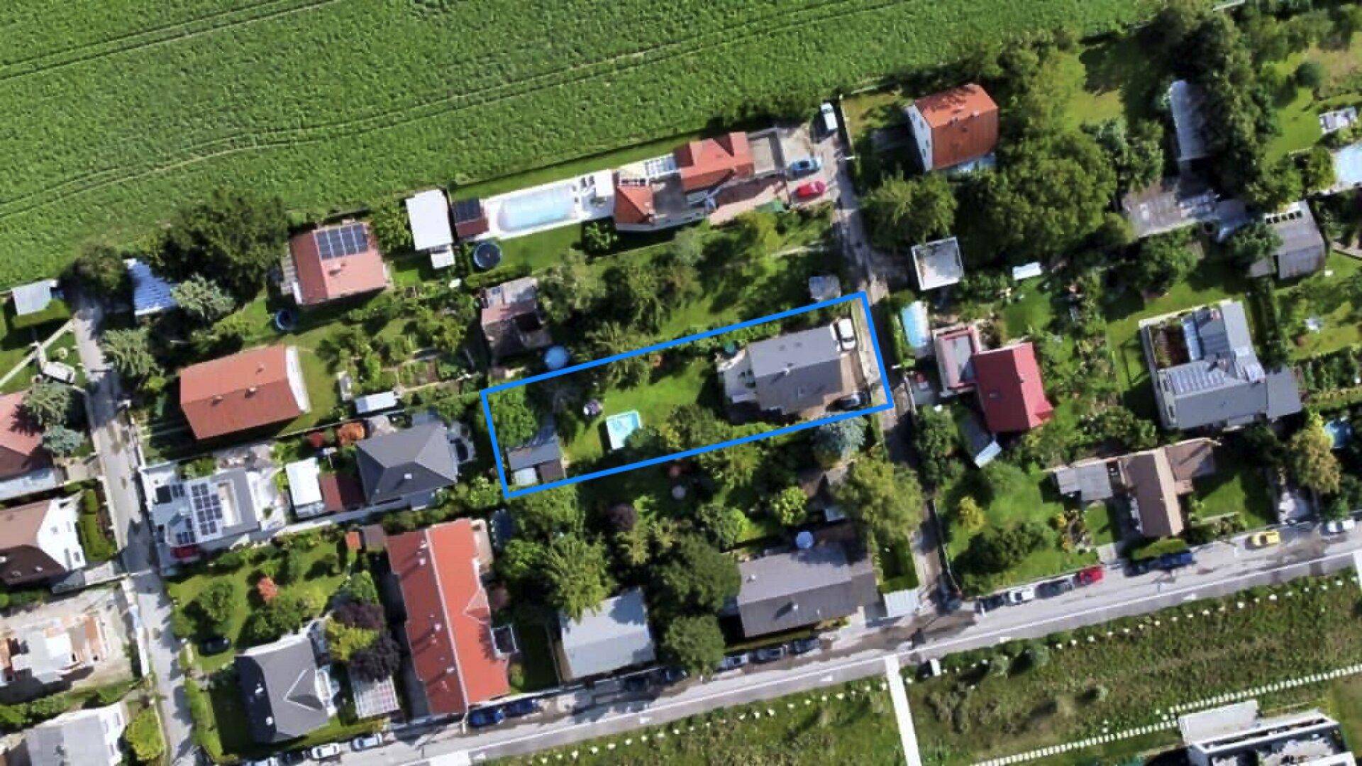 Luftaufnahme eines Wohngebiets mit einem blau umrandeten Grundstück und angrenzenden Feldern.